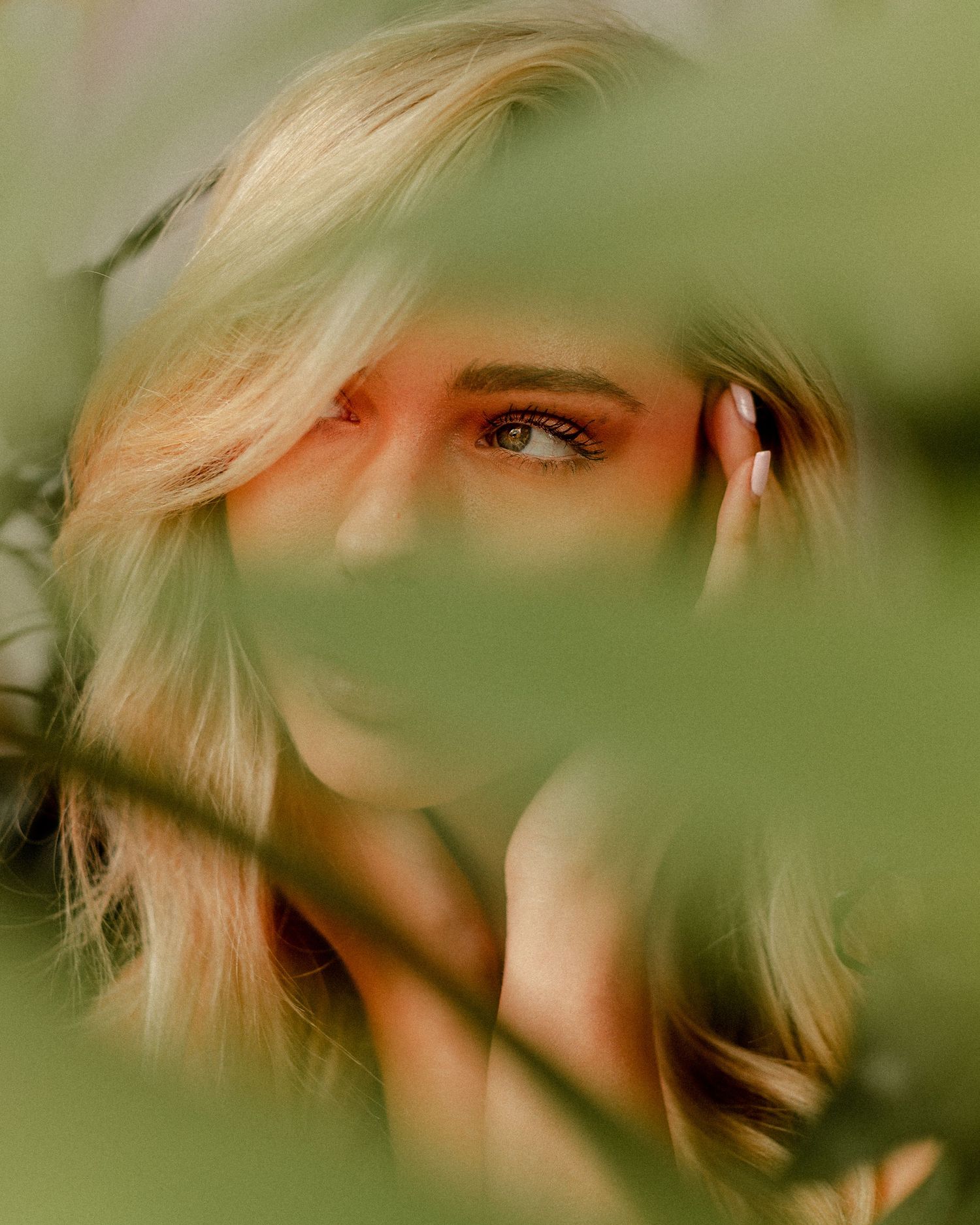 Artistic beauty shot with face partially obscured by green foliage.