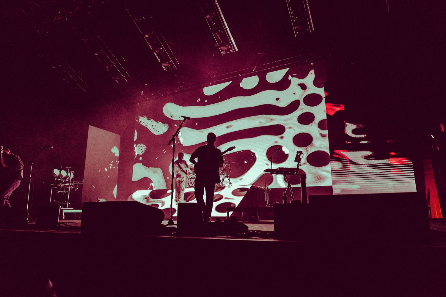 A dark stage illuminated with red lighting and silhouetted performers during a theatrical performance.