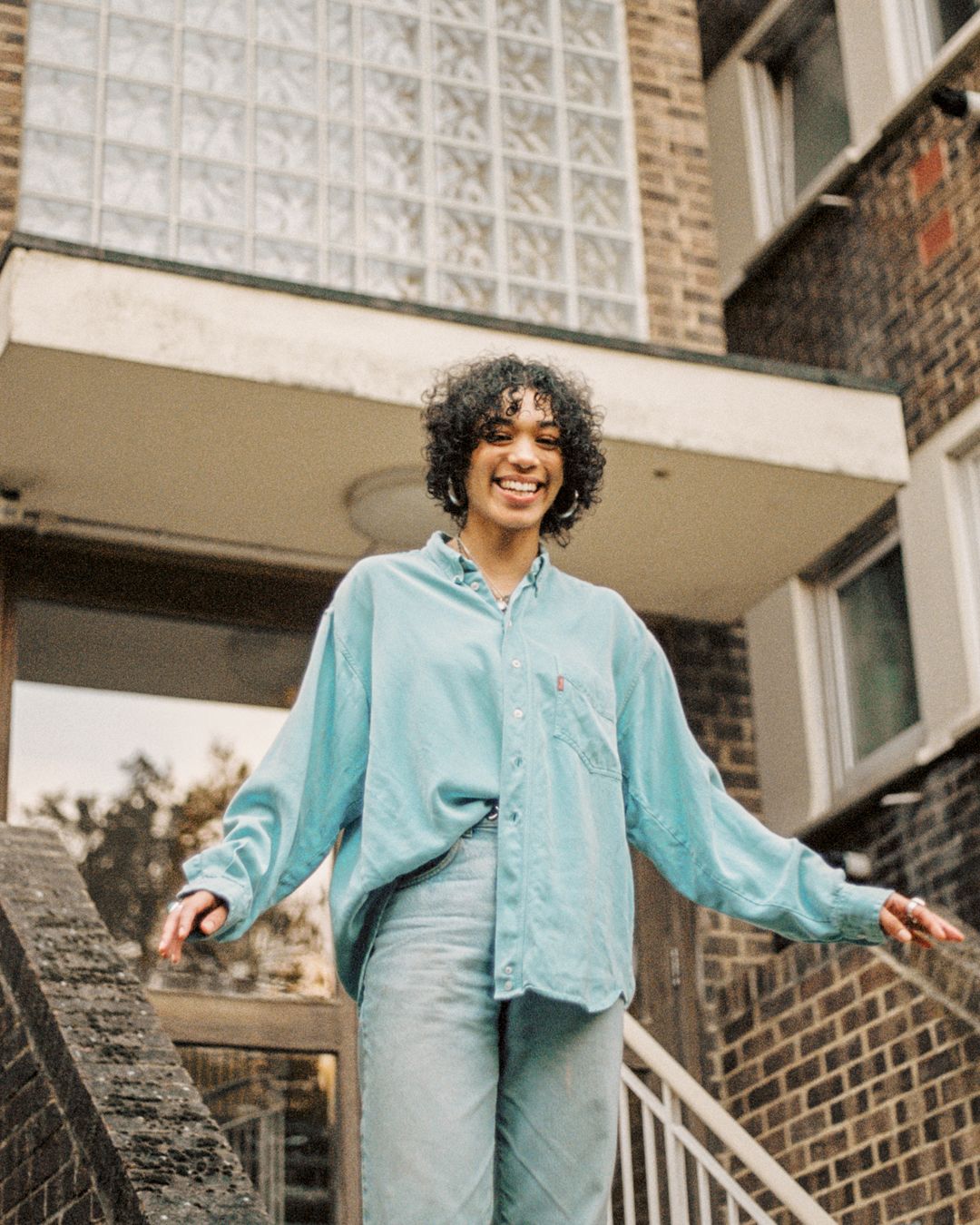 Candid fashion shot on building steps wearing oversized mint shirt and light jeans.