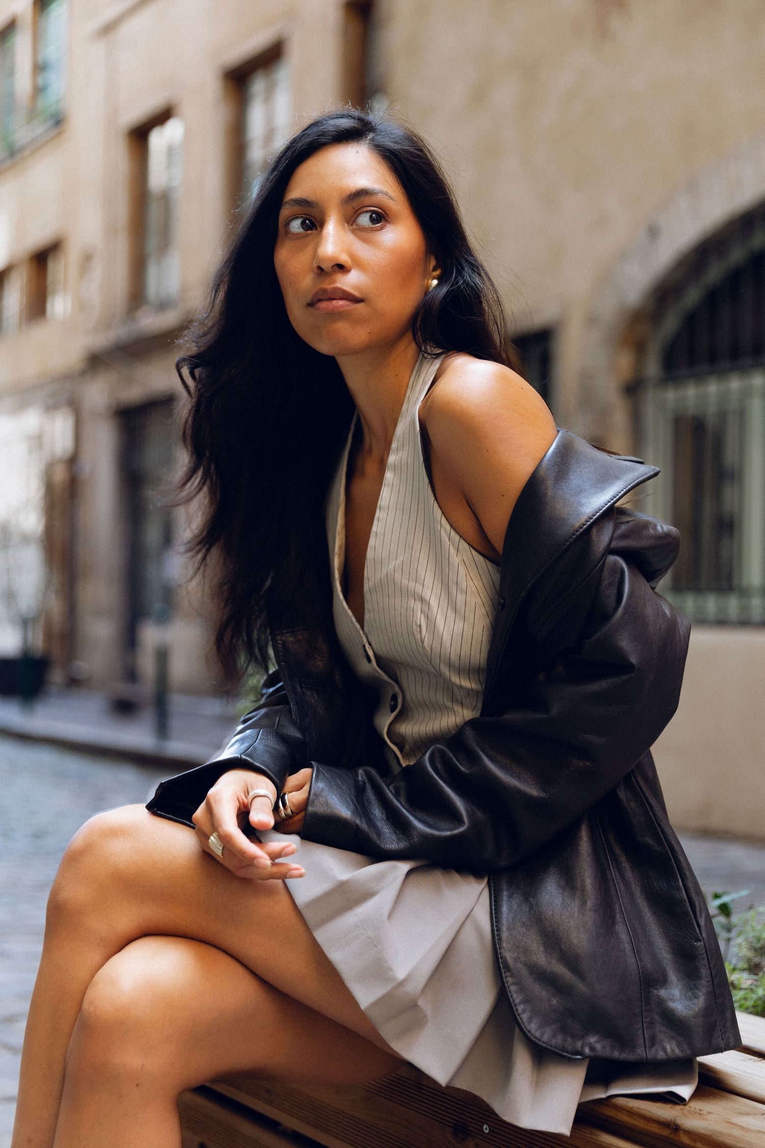 Street style fashion photo featuring leather jacket and cream dress in urban setting.