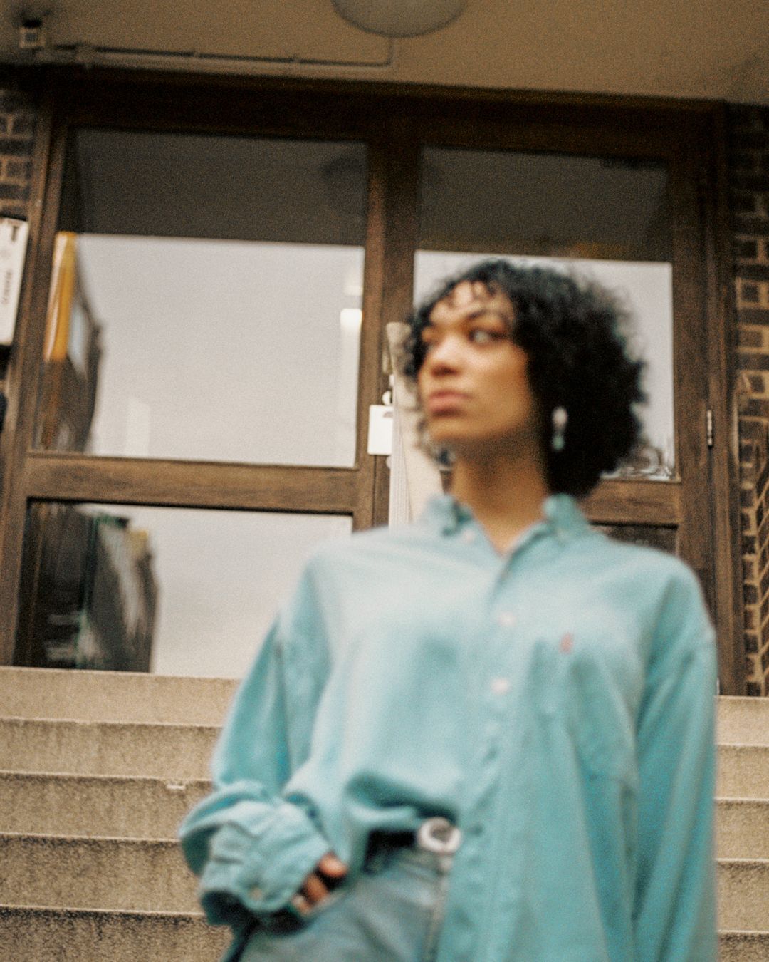 Person in oversized mint button-down shirt poses near architectural doorway.