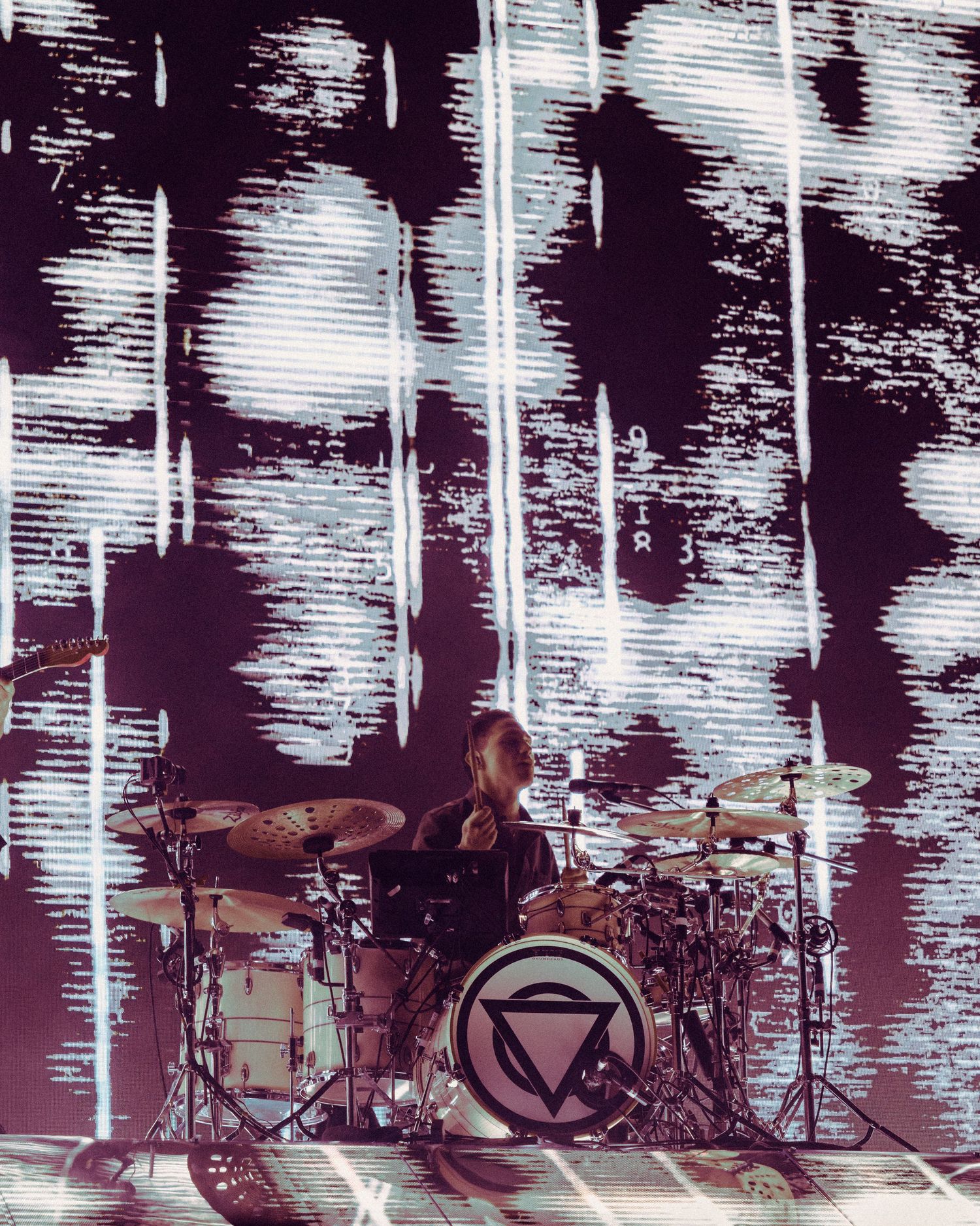 Row of multiple drum sets on stage with dramatic black and white backdrop lighting display during live performance.