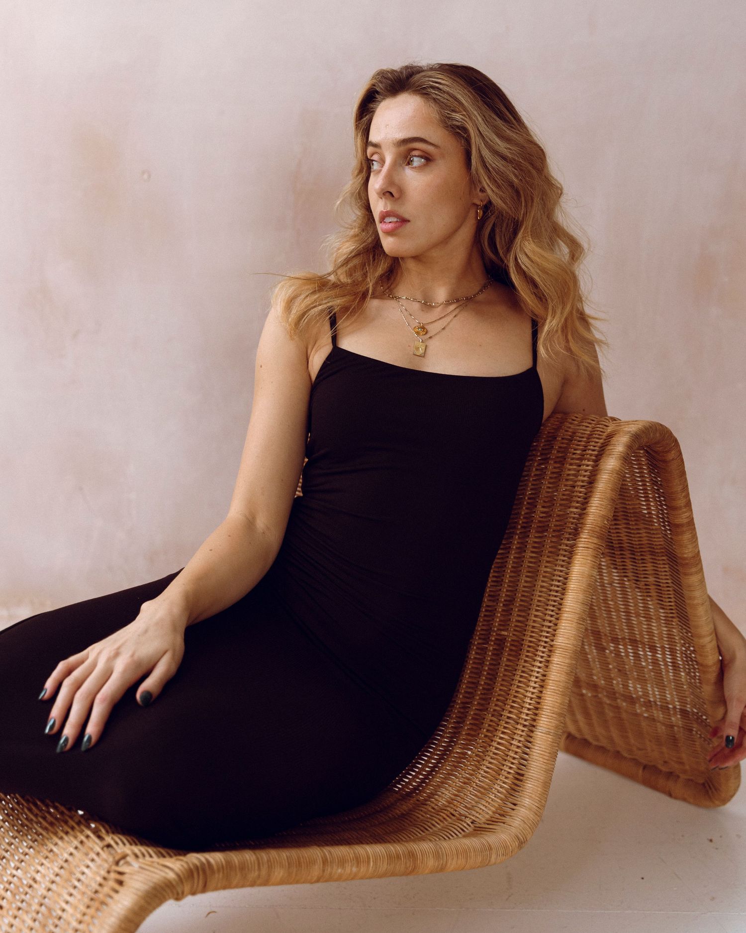 Artistic fashion photography featuring model lounging in wicker chair wearing black outfit.