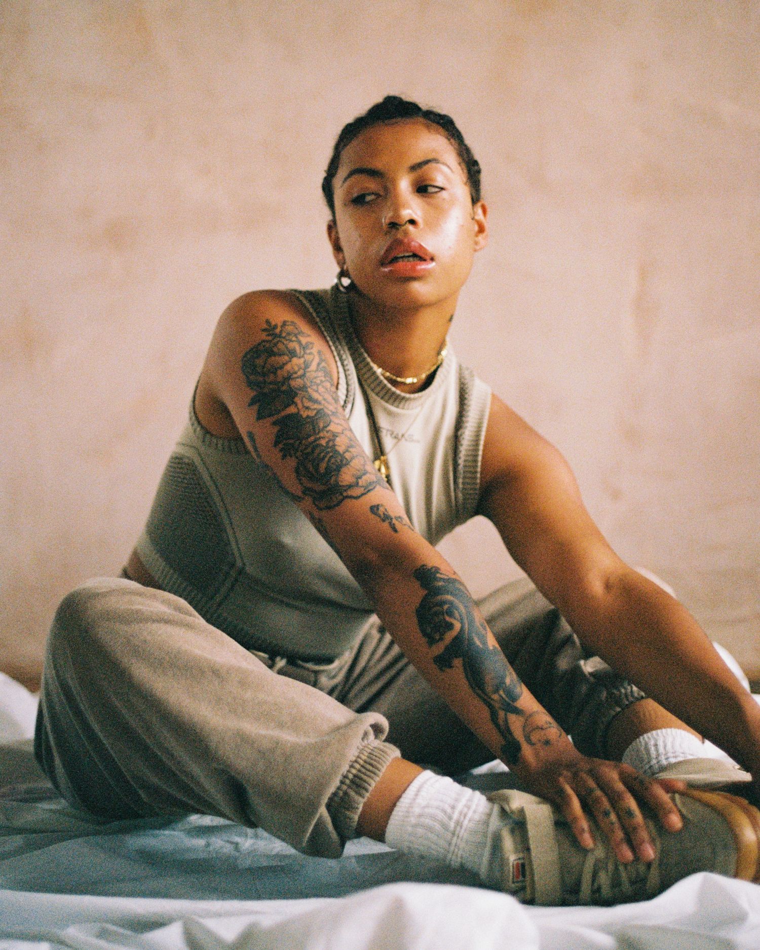 Casual portrait on bedding showing detailed tattoo sleeve and relaxed pose.