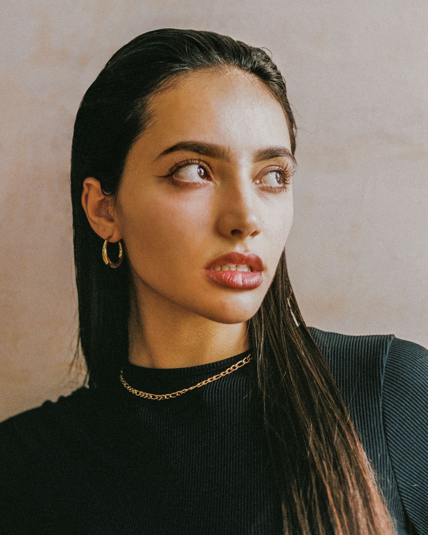 Side-glancing portrait with gold jewelry and sleek dark hair.