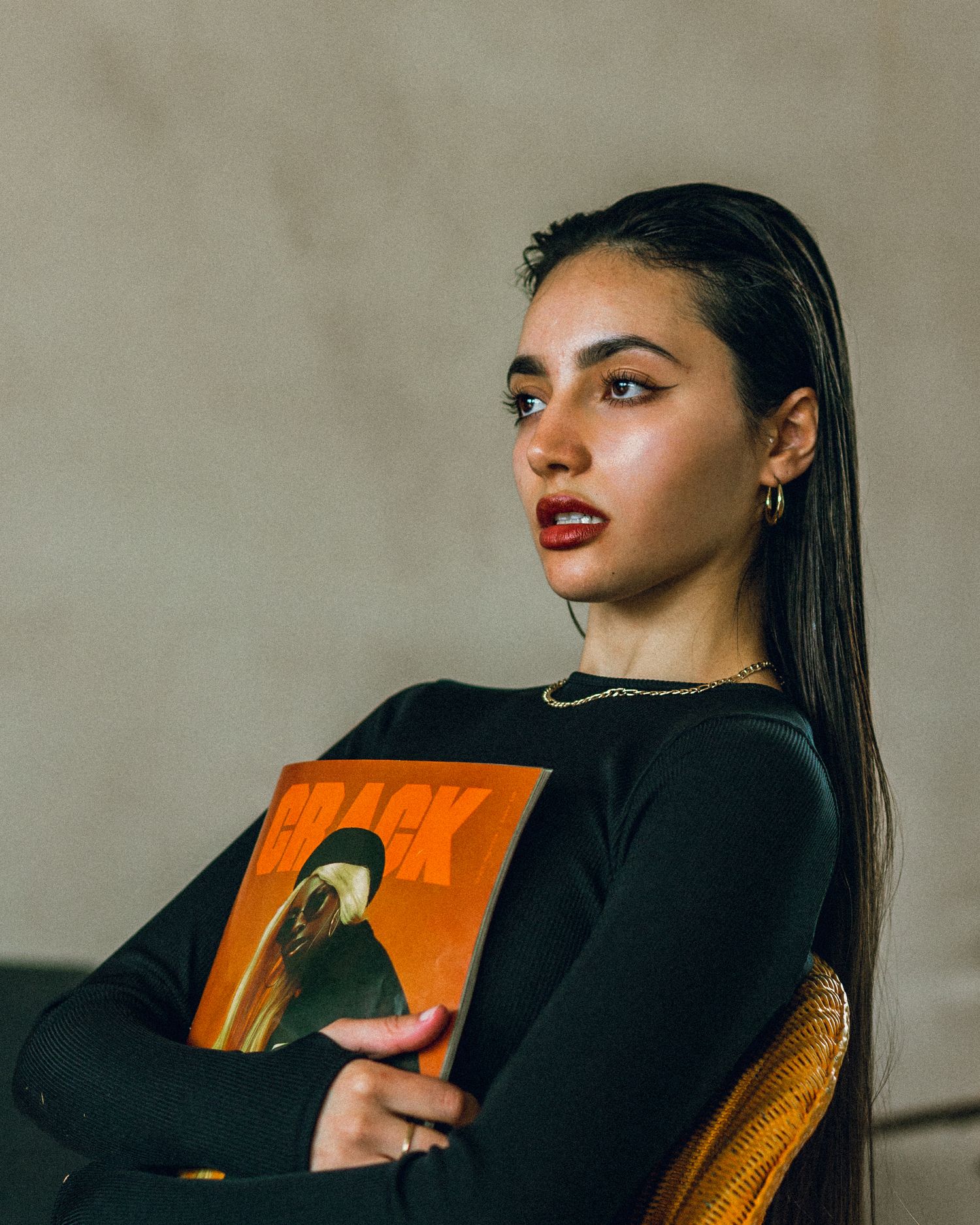 Stylish portrait holding orange album cover while seated in yellow rattan chair.