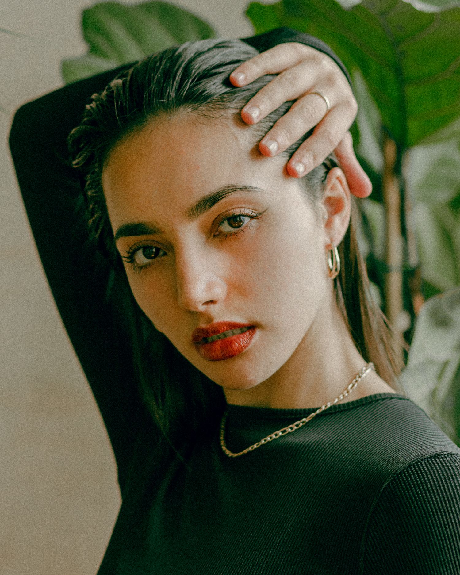 Portrait with tropical plant backdrop featuring sleek hair and gold jewelry.