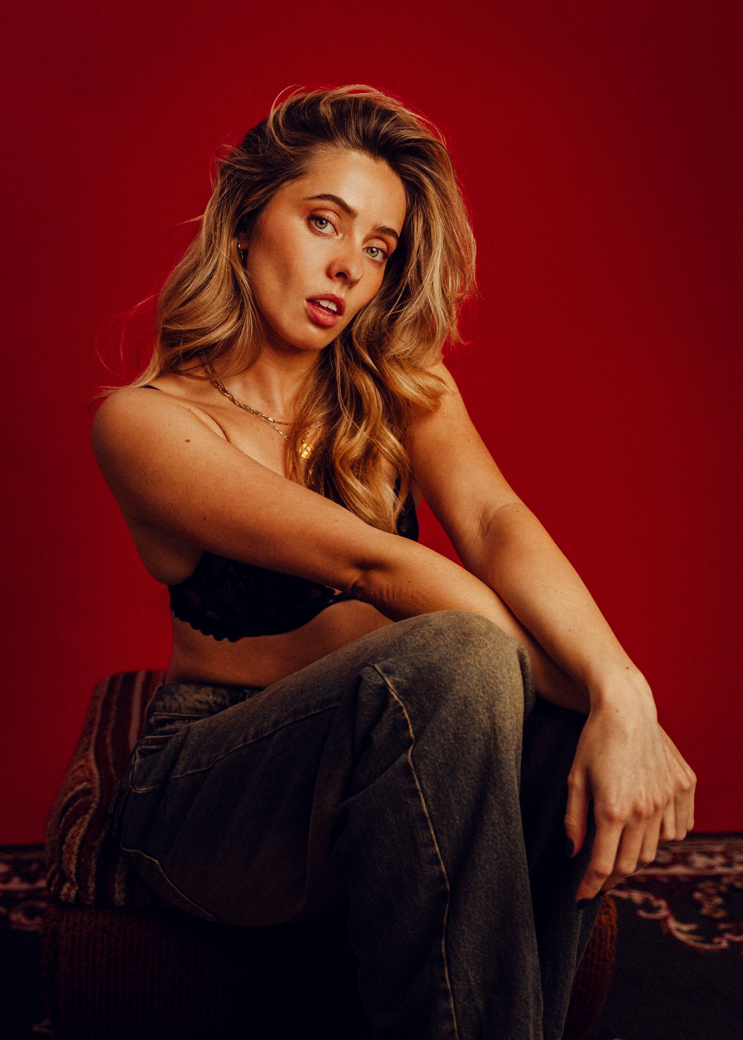 Fashion editorial shot features casual styling against dramatic red studio backdrop.