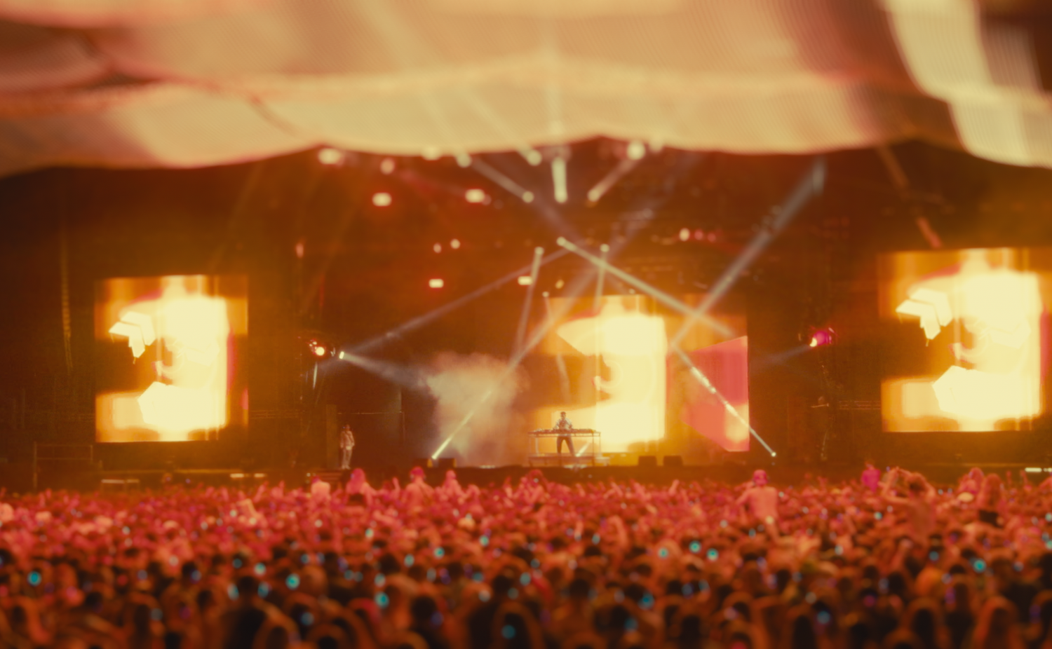 Concert stage lit up with fire effects and massive crowd in foreground.