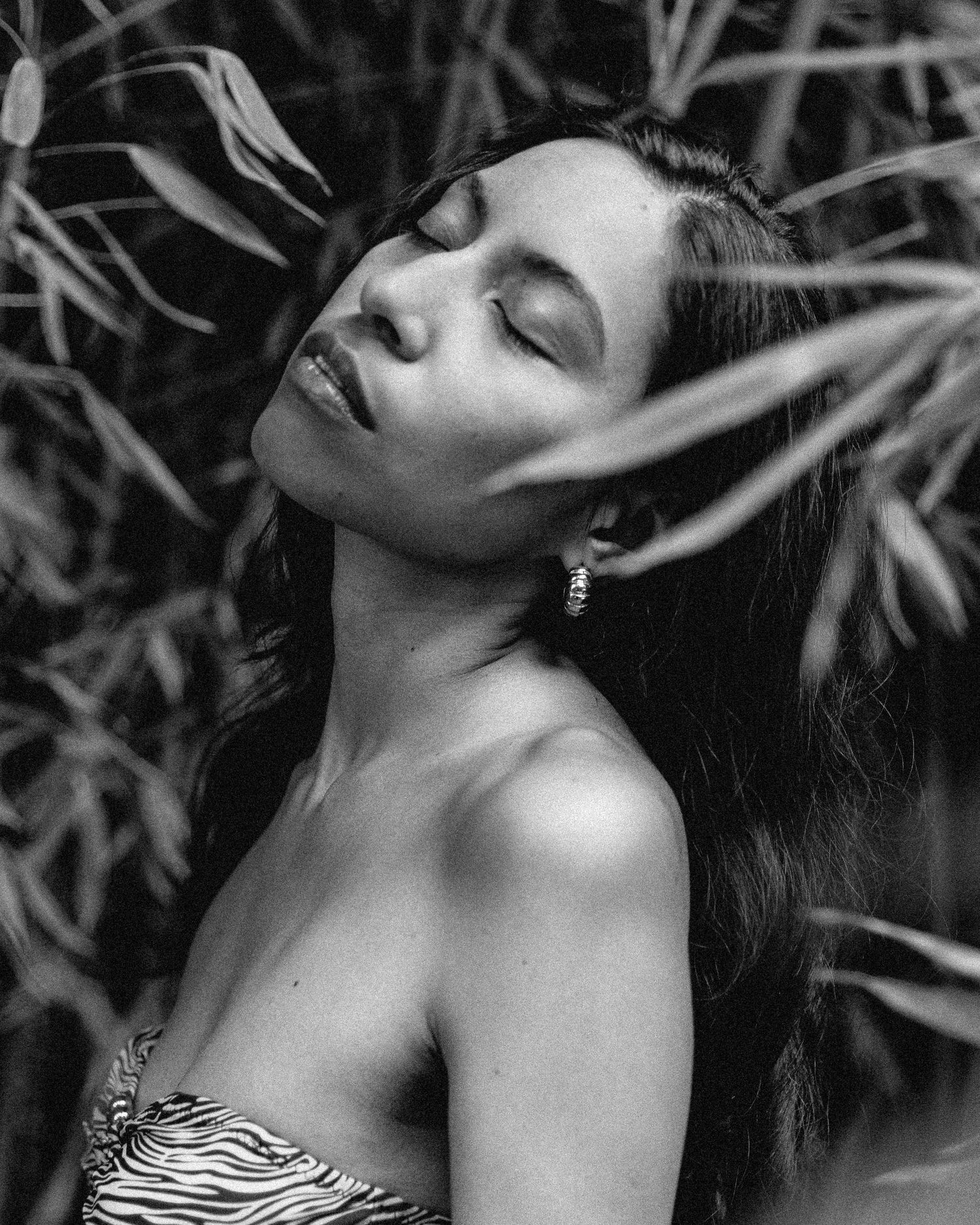 Artistic black and white portrait with bamboo leaves creating dramatic shadows.