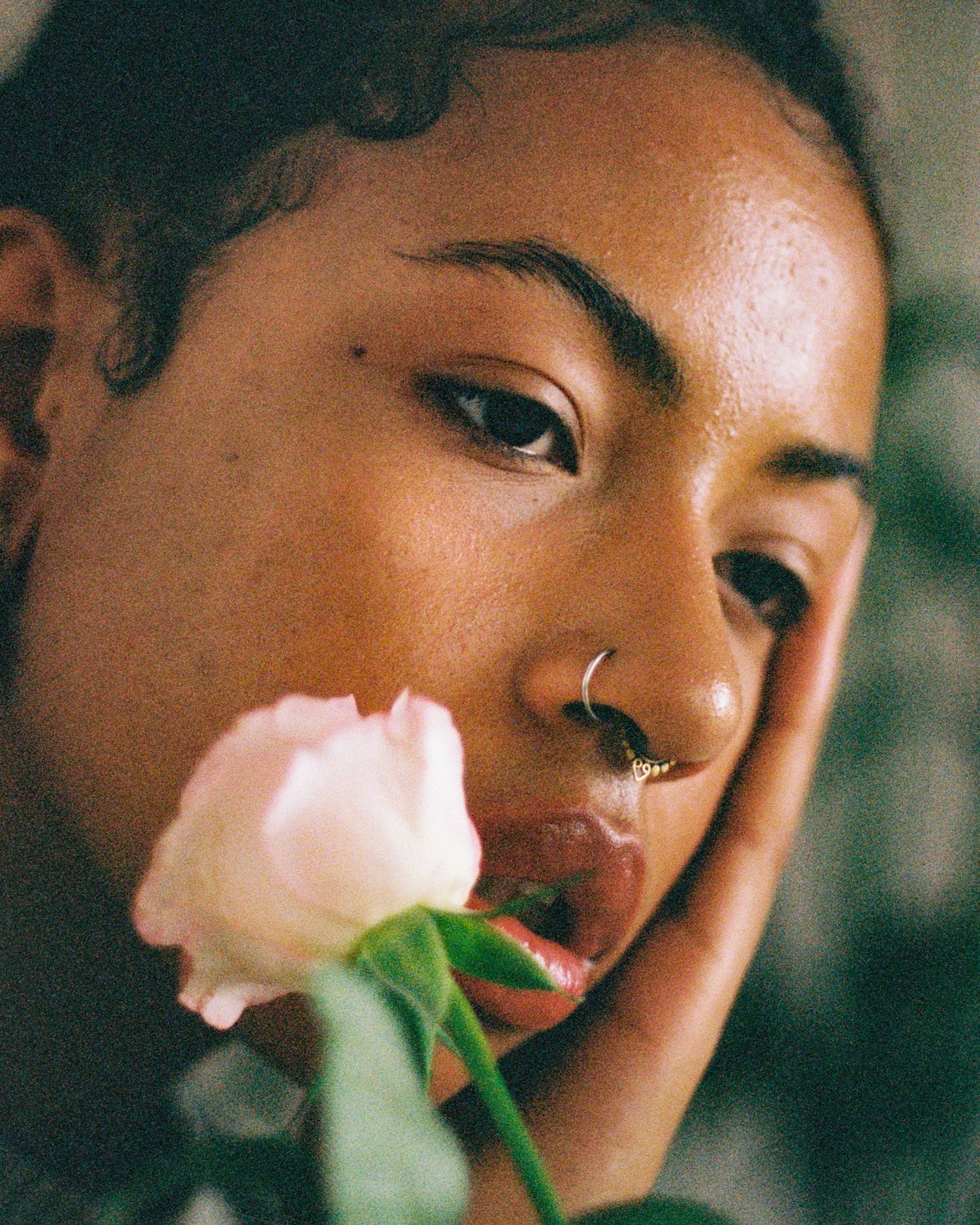 Dreamy close-up portrait with pink rose and nose piercing.