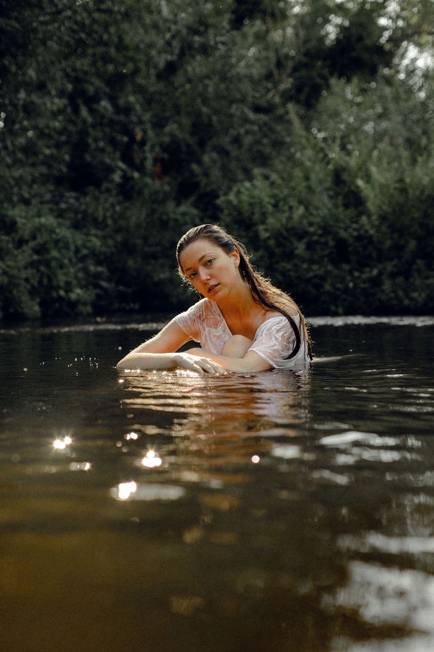Figure floating gracefully in dark water with sunlight creating sparkles on the surface.