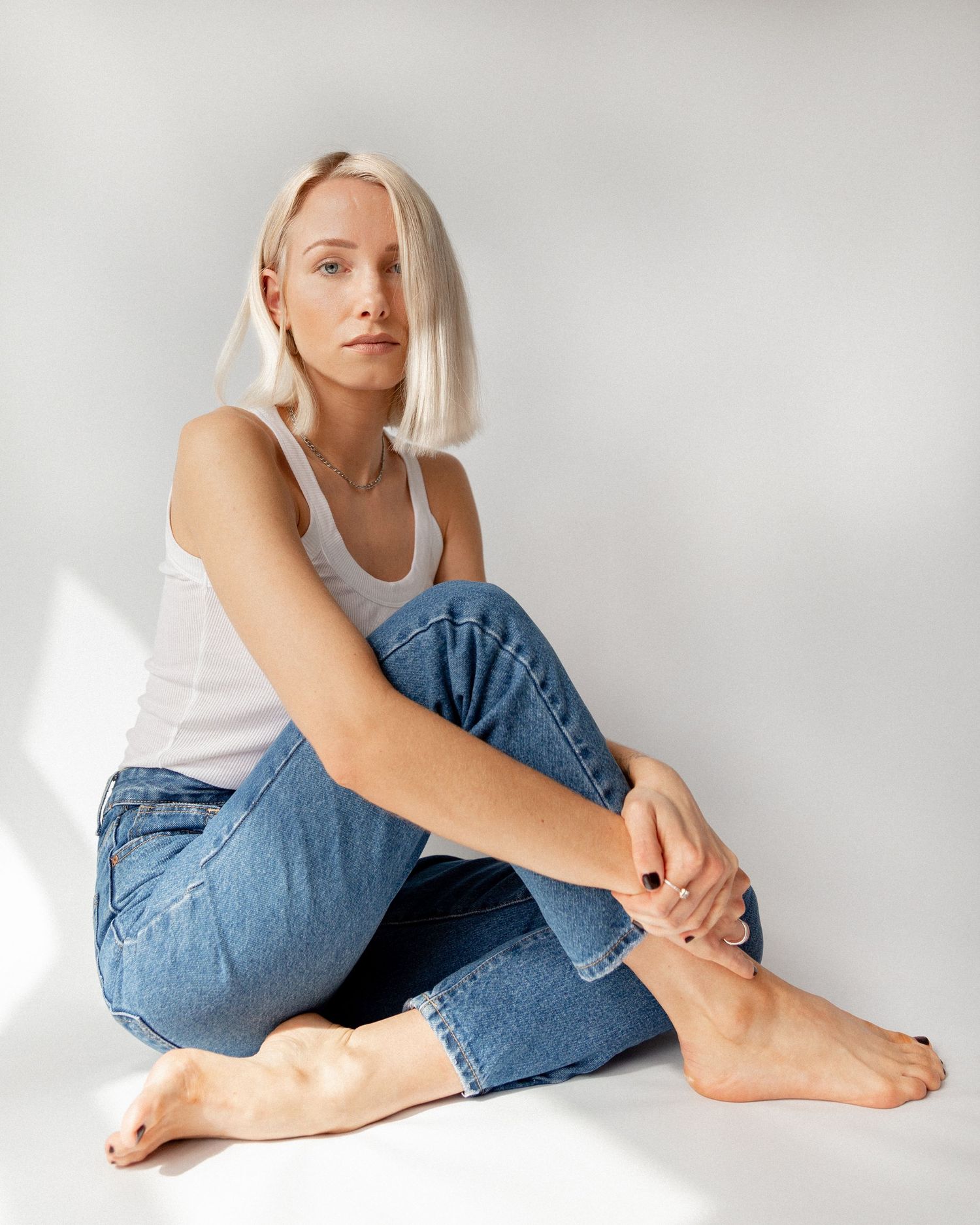 Casual lifestyle portraits in white tank top and blue jeans against minimalist white background.