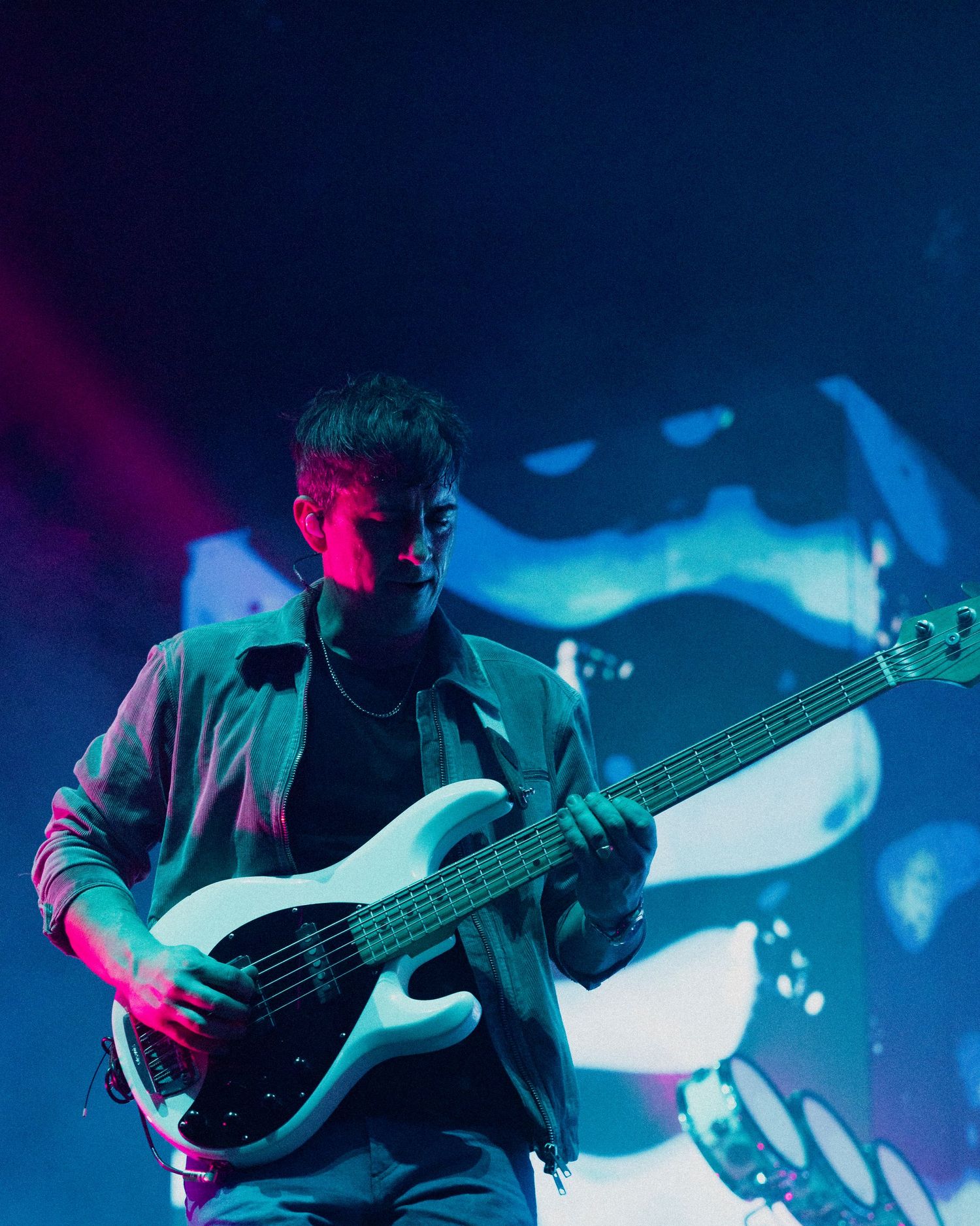 Bass guitarist performing on stage illuminated by vibrant blue and pink stage lighting during a concert performance.