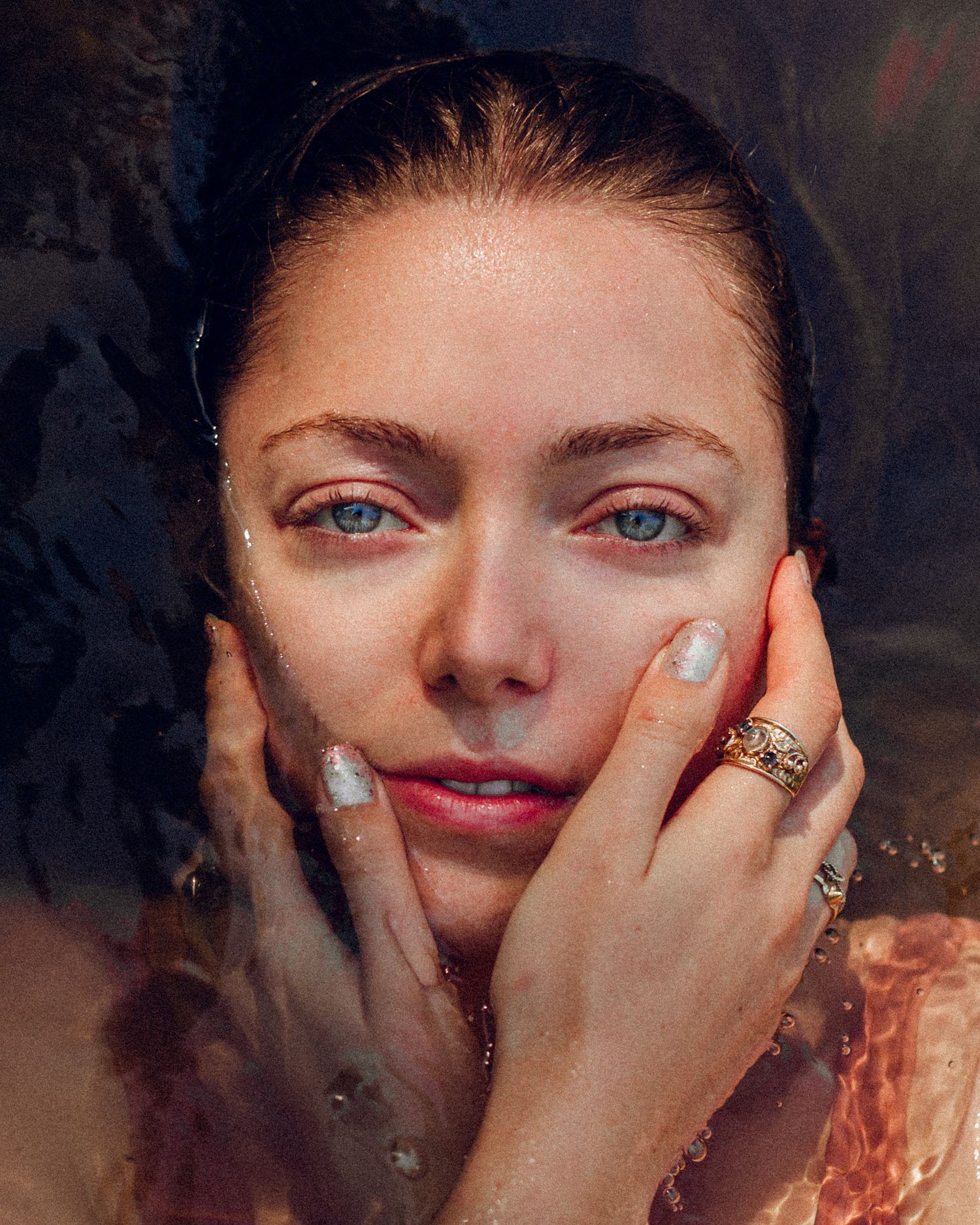 Close-up portrait with hands framing face in warm dramatic lighting.