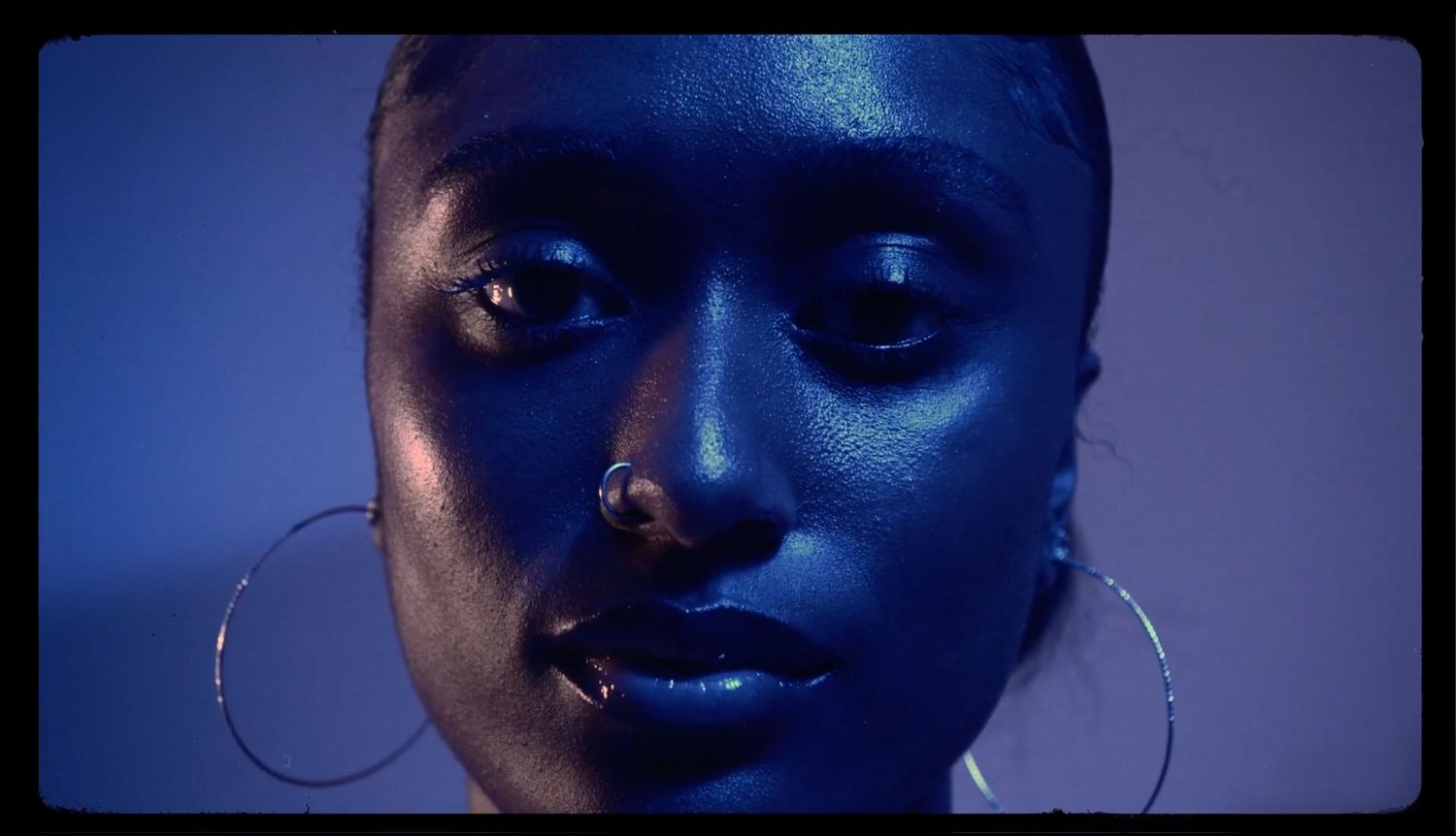Artistic close-up portrait with deep blue lighting and silver hoop earrings.