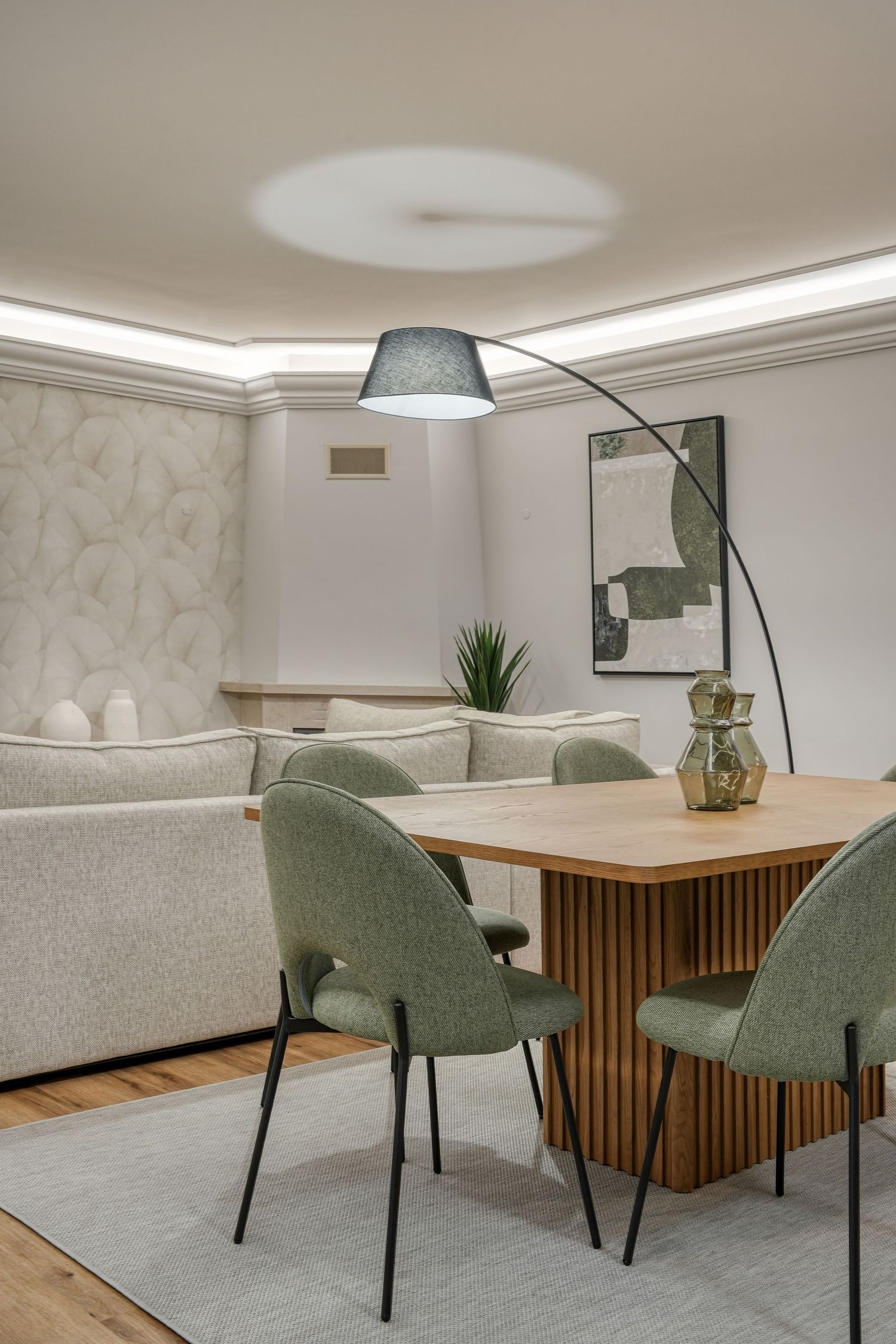 Modern dining area with sage green chairs around a wood table, arc lamp, and cozy living space with neutral tones.