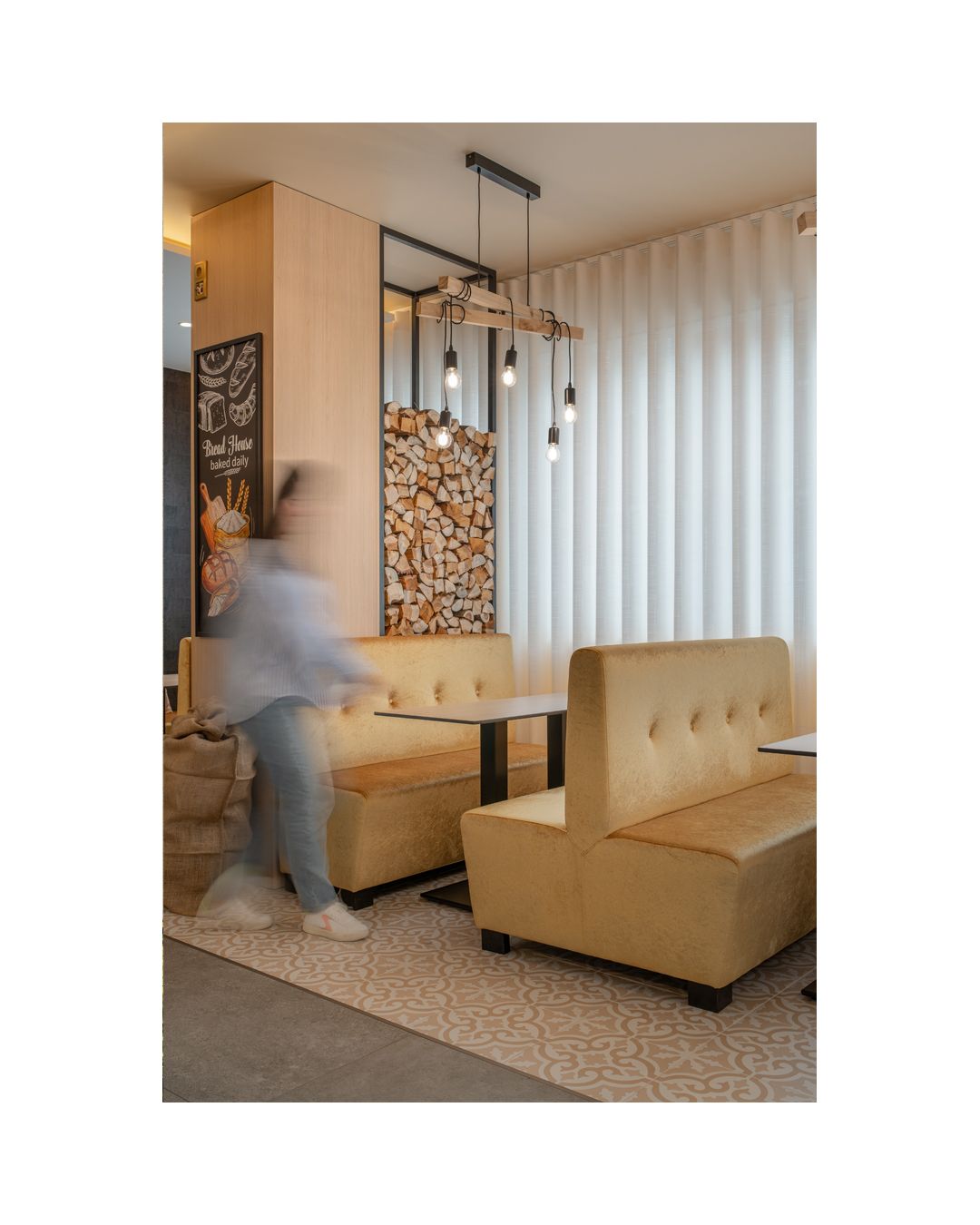 Contemporary dining area with beige banquette seating and decorative stacked firewood display.