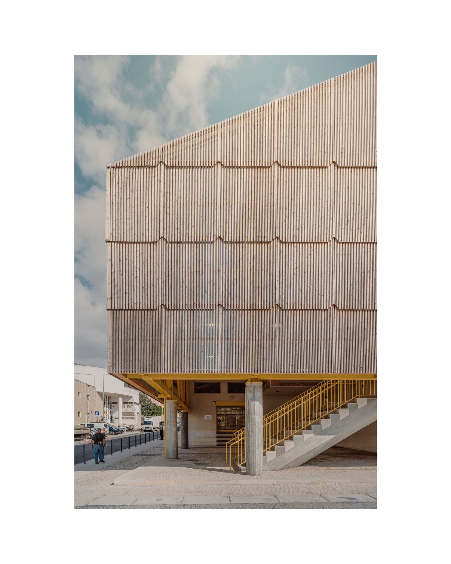 Modern building exterior featuring wooden shingle cladding and a concrete staircase entrance against a cloudy sky.