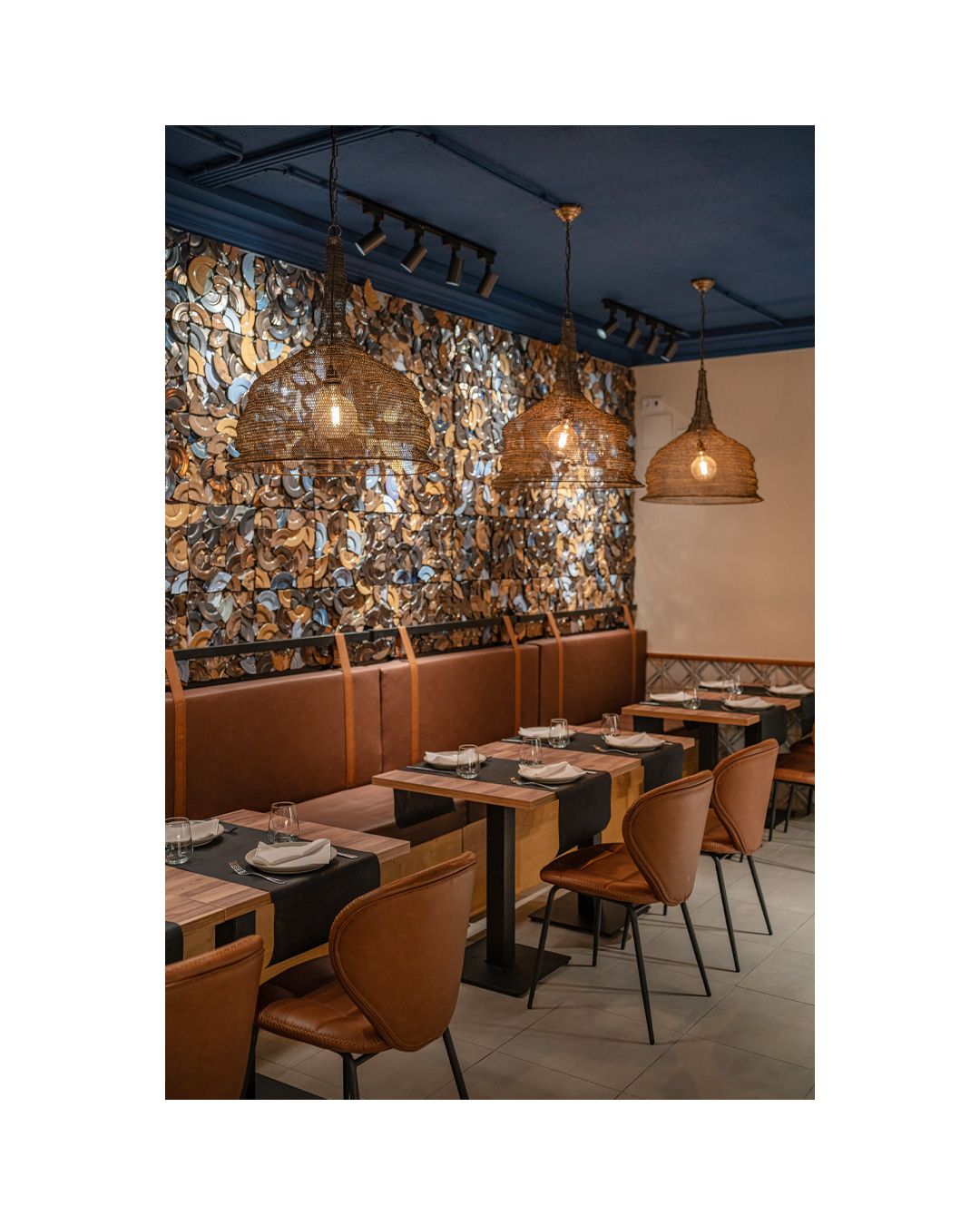 Modern restaurant interior with patterned wallpaper, pendant lights and brown leather seating.
