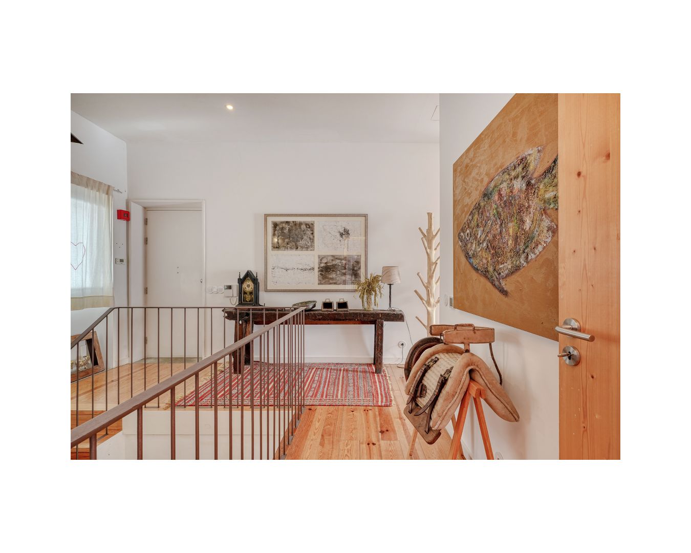 Upper landing hallway featuring artwork, wooden console table, and metal railing details.