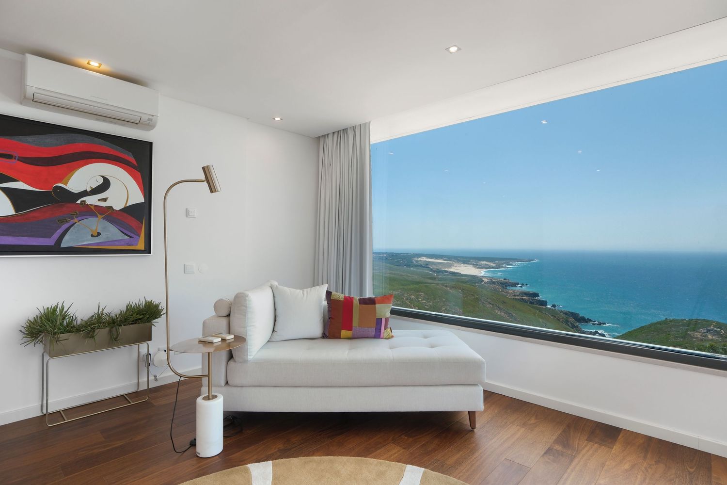 Modern coastal bedroom with panoramic ocean views, white daybed, and contemporary red artwork.