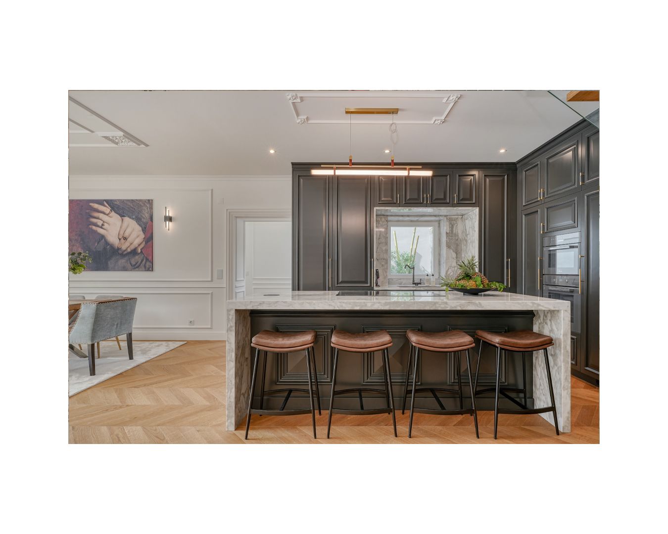 Modern kitchen with dark cabinets, leather bar stools, and herringbone wood flooring.