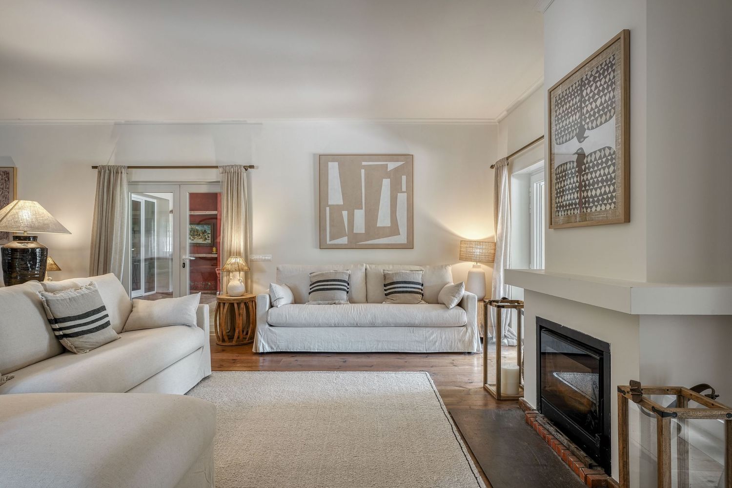Bright living room with white sofas, fireplace, hardwood floors, and neutral decor in an elegant home.