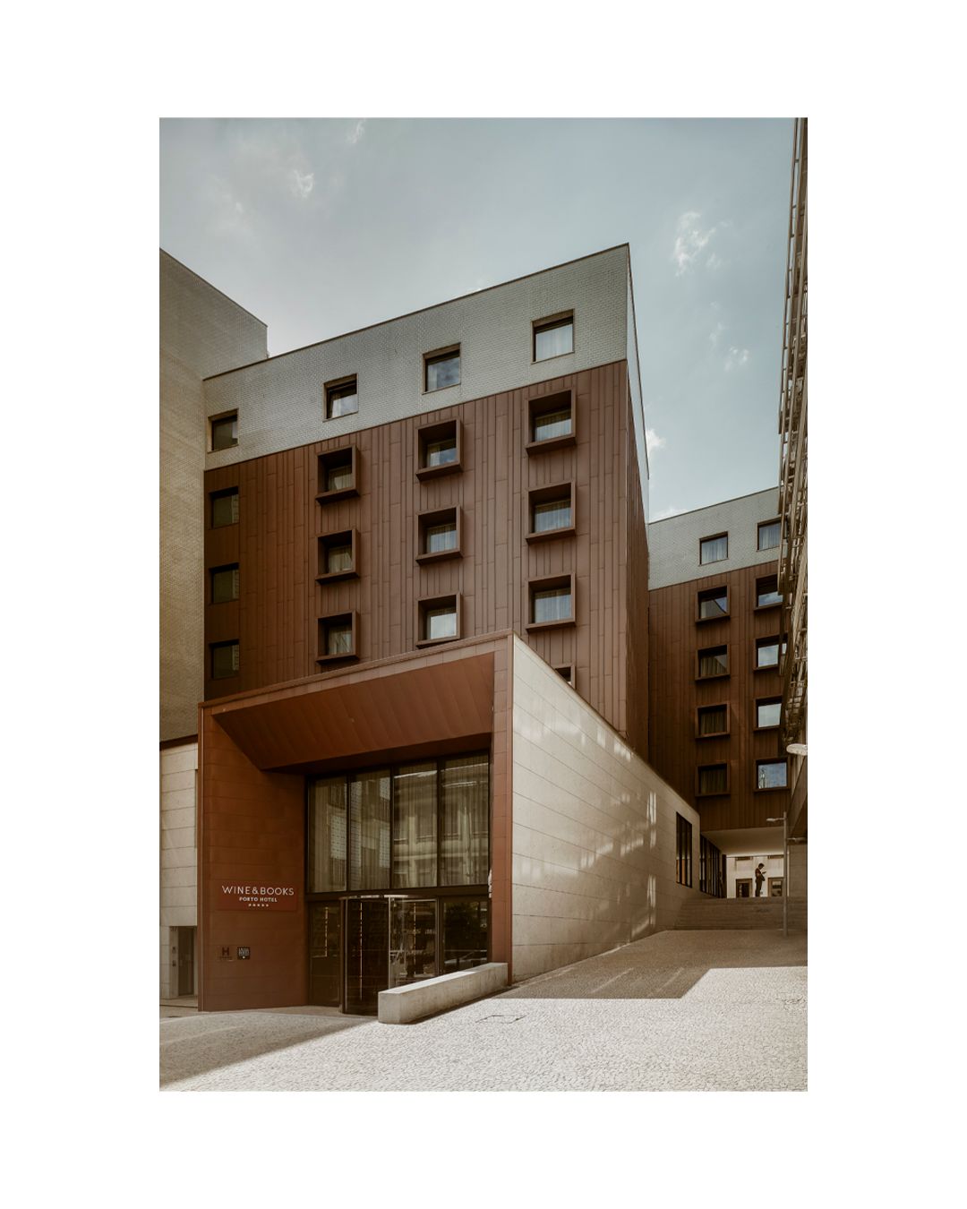 Modern apartment building exterior with brown wood panels and rectangular window pattern.