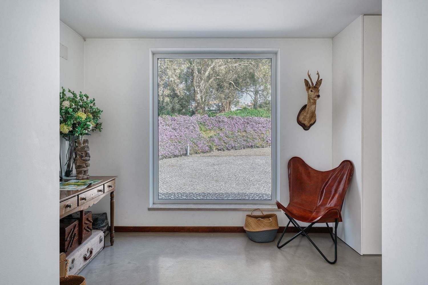 Minimalist sitting room with leather butterfly chair, large window overlooking lavender garden, and antelope wall mount.