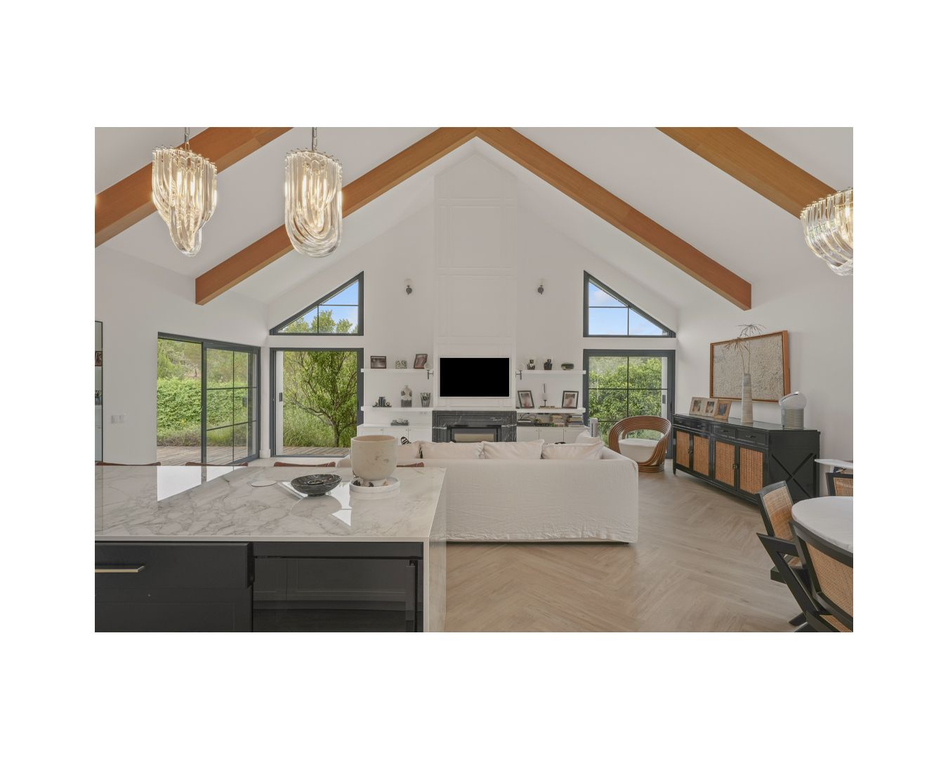 Open-concept living space with vaulted ceiling, exposed beams, and large windows offering natural light.
