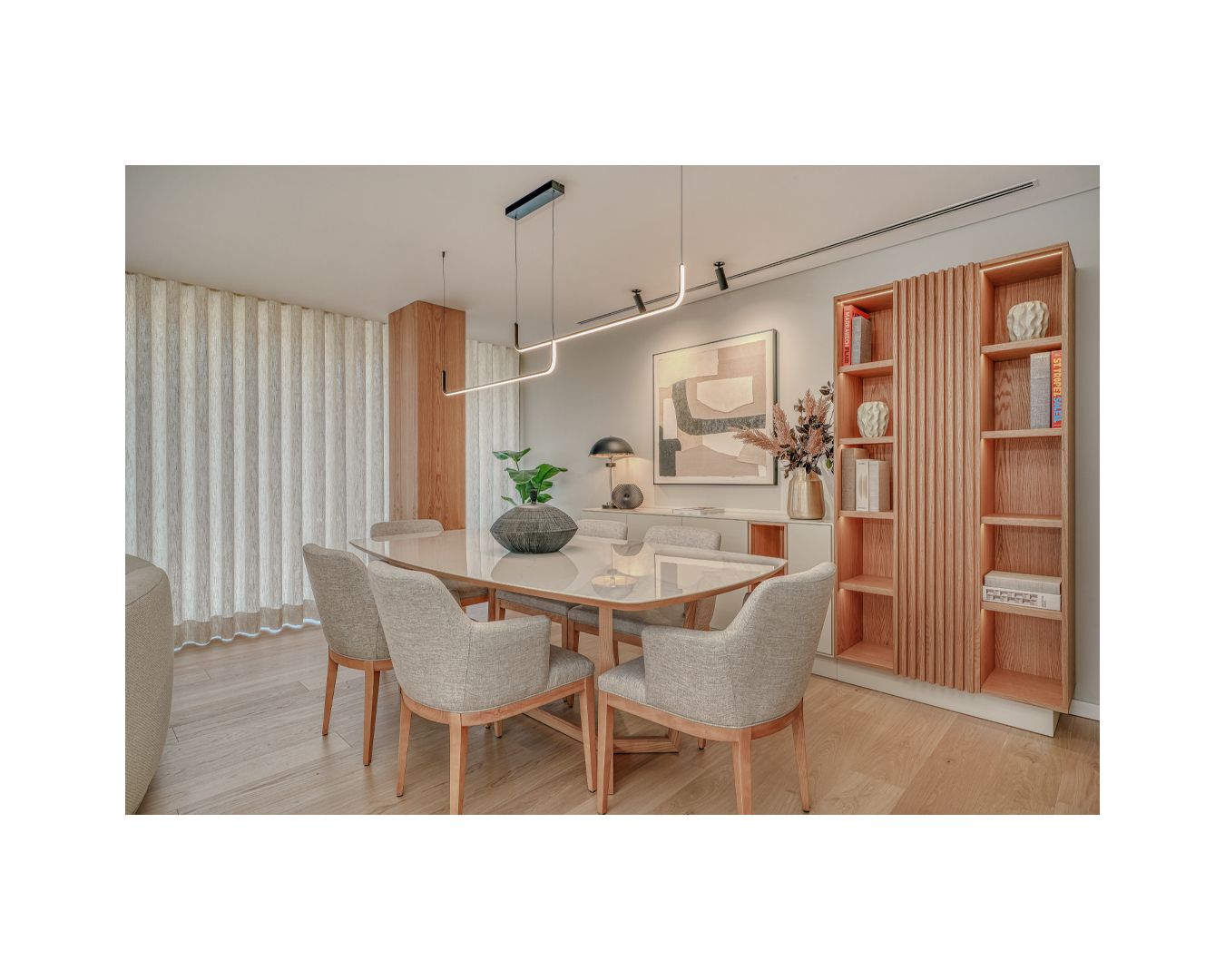 Contemporary dining area with beige chairs, wooden table, and built-in shelving in warm tones.