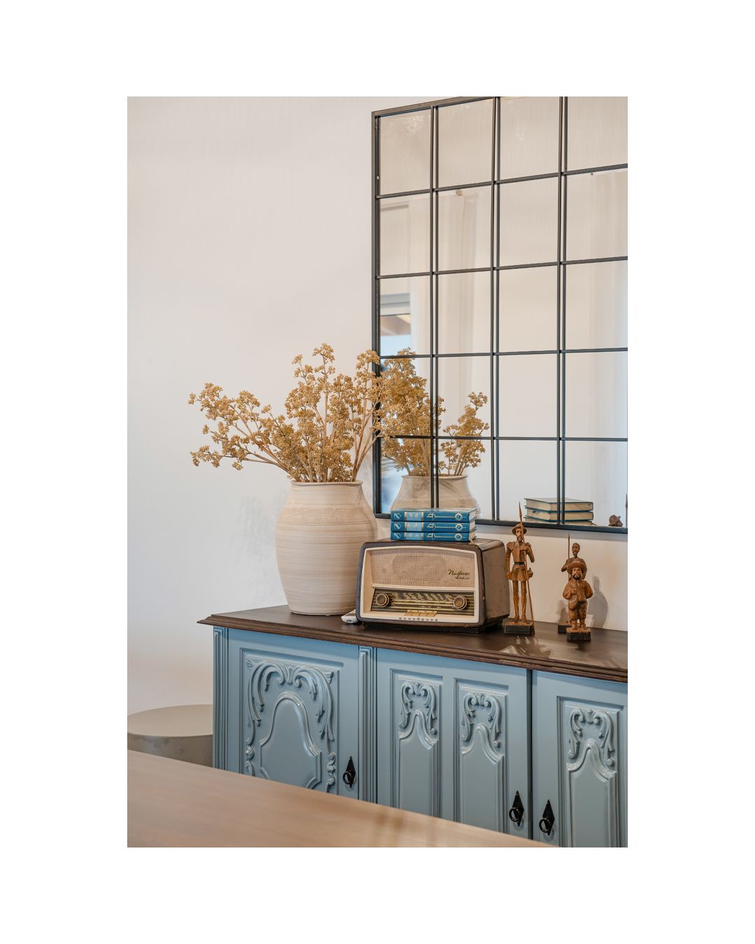 Vintage-inspired blue cabinet with decorative panels styled with books and dried flowers.
