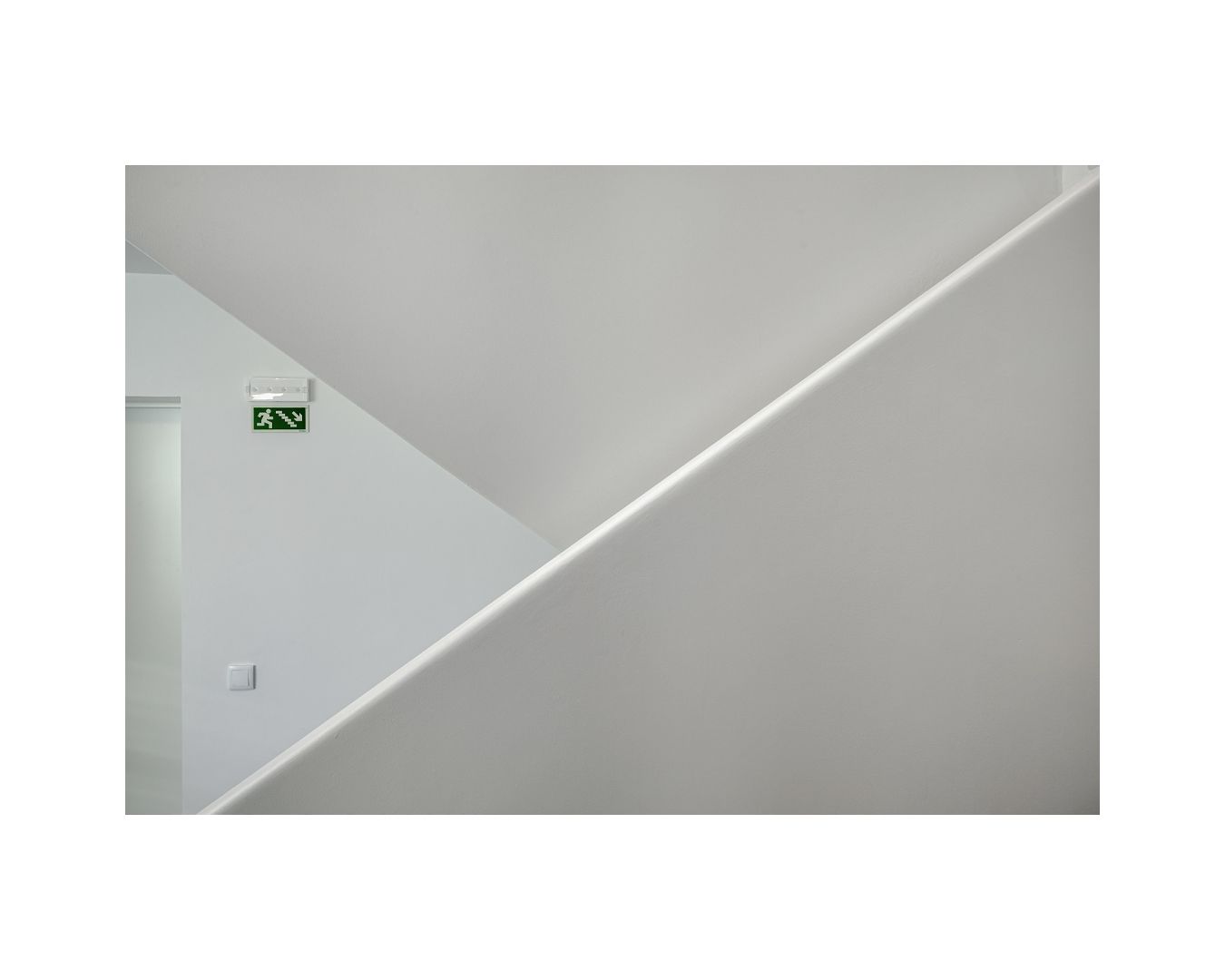 Minimalist white interior hallway with diagonal LED light fixture and emergency exit sign.
