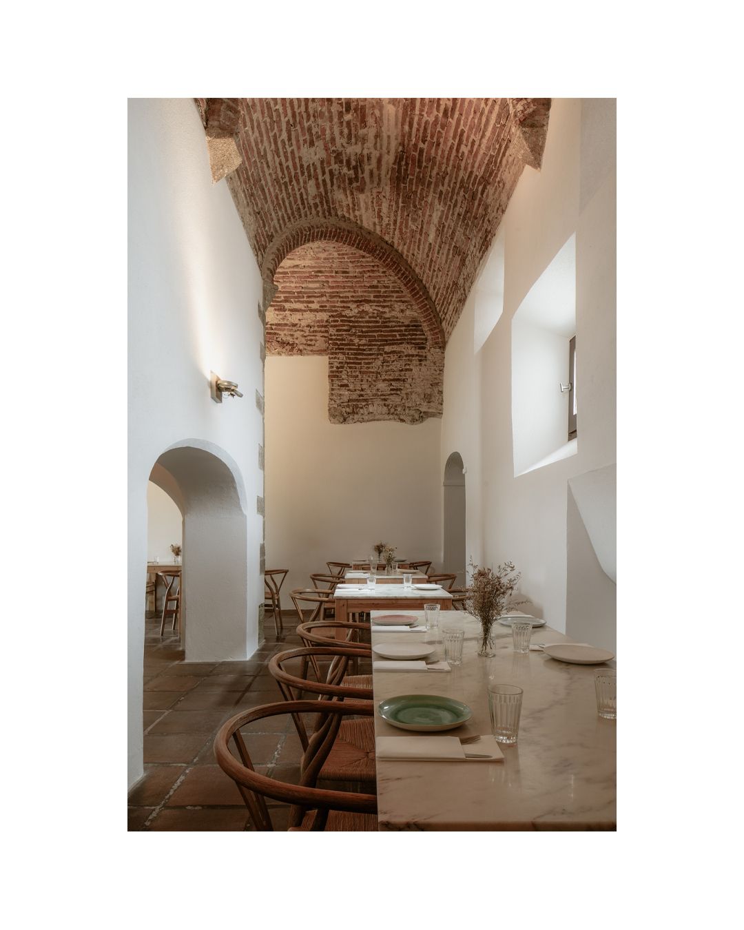 Rustic dining room with exposed brick ceiling, white walls, and elegant table settings.