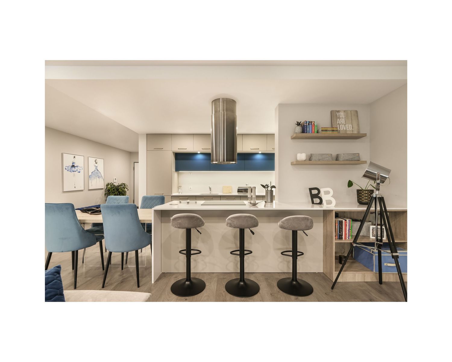 Modern dining area with blue chairs and pendant lighting in a minimalist white kitchen space.