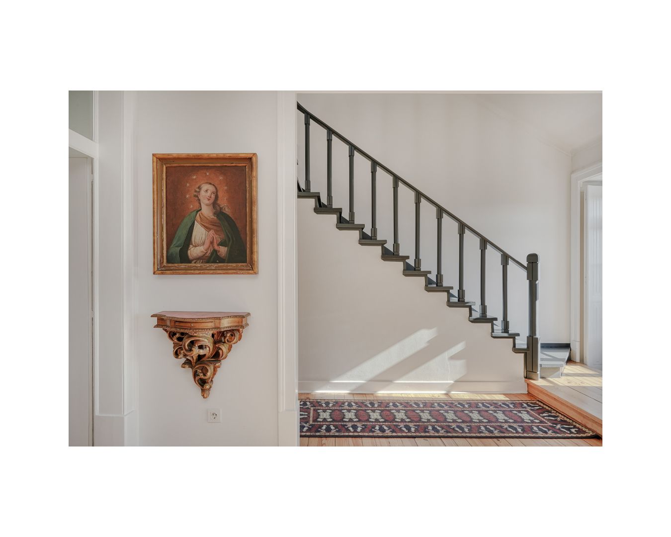 Elegant staircase with iron railings and decorative artwork on white walls.