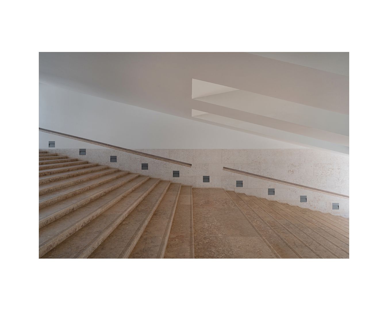 Modern minimalist auditorium with curved wooden seating rows and white walls stretching upwards in an empty space.