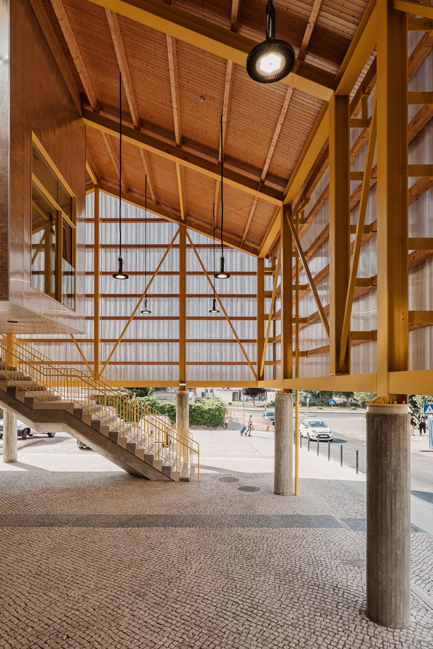 Interior view of a modern wooden pavilion structure with exposed beams and cobblestone flooring underneath.