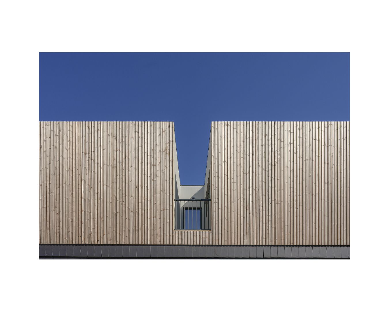 Minimalist wooden facade with a geometric gap in the center against bright blue sky.