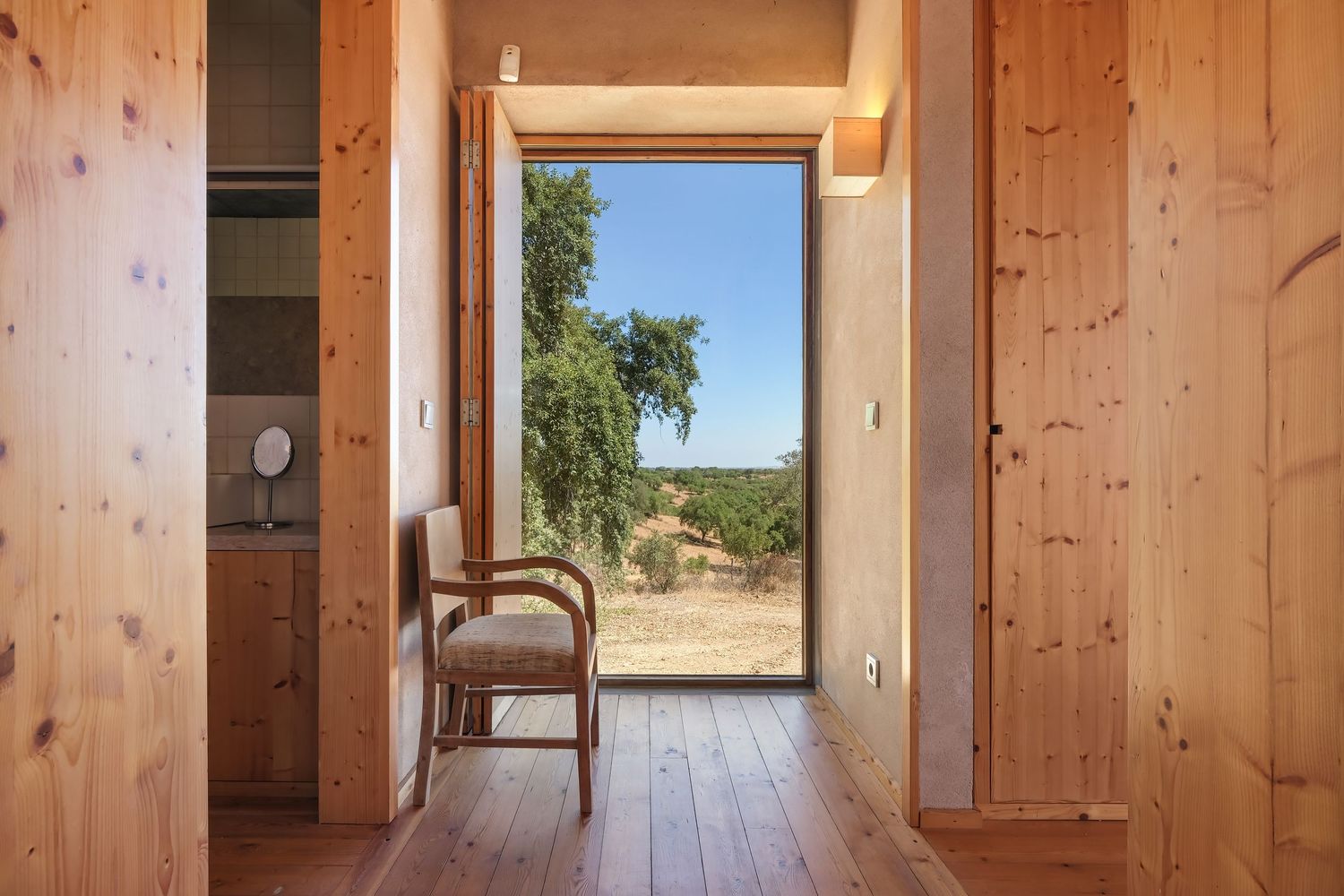 Rustic wooden hallway with natural light streaming through window, showcasing countryside view.