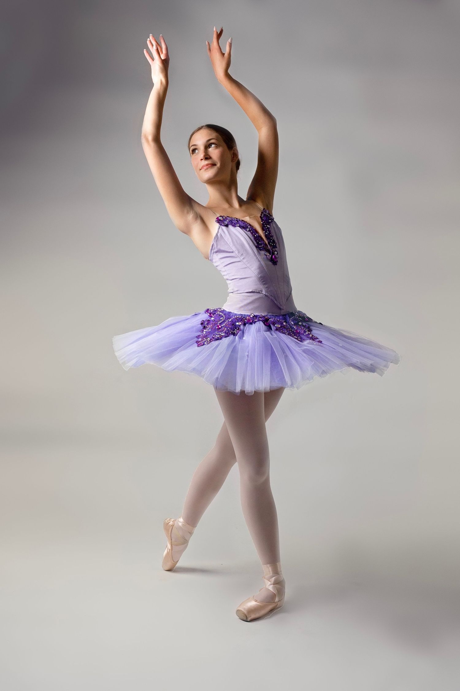 Ballerina in purple tutu performs classical ballet positions in studio setting.
