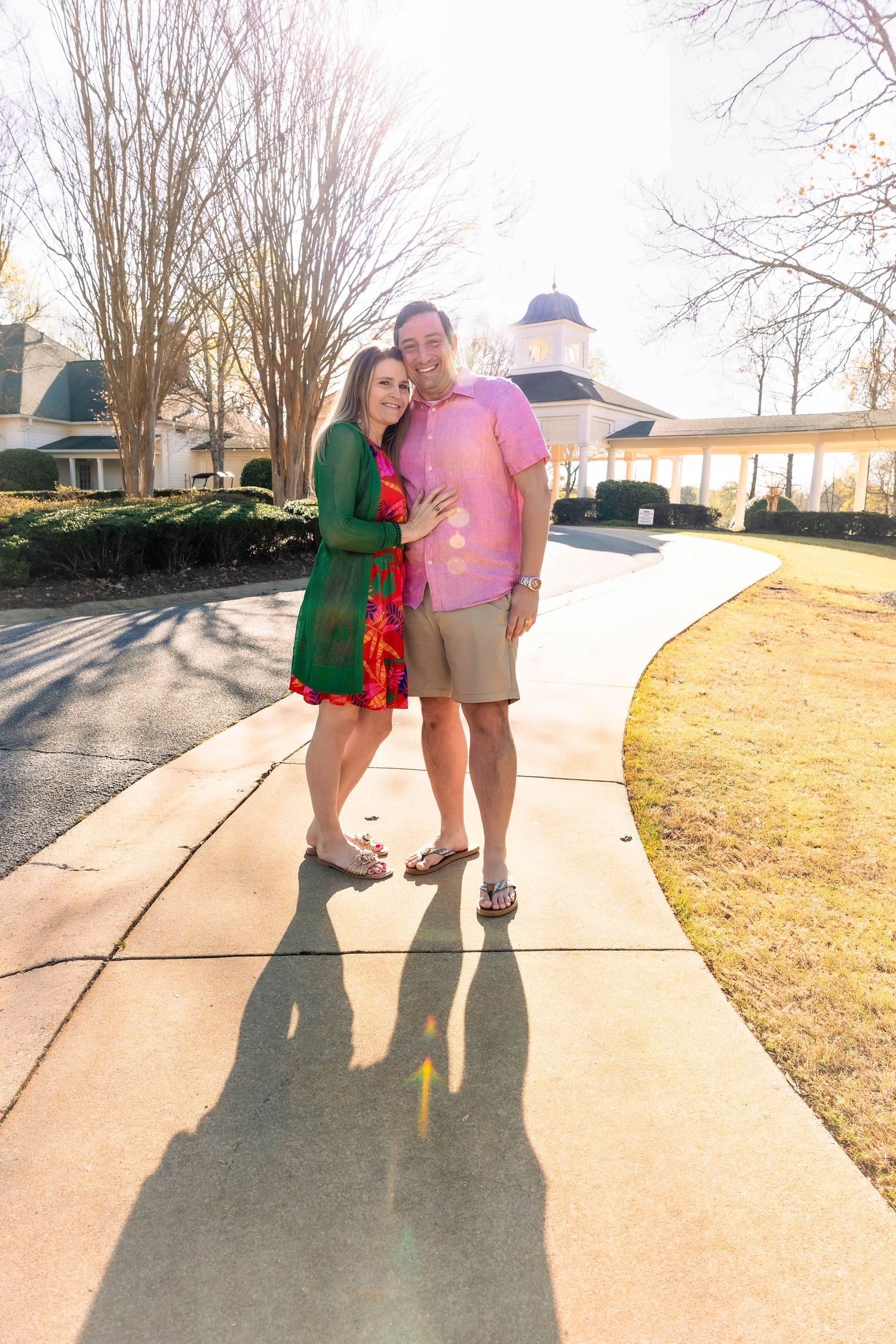 Couple walking together on sunny sidewalk casting long shadows.