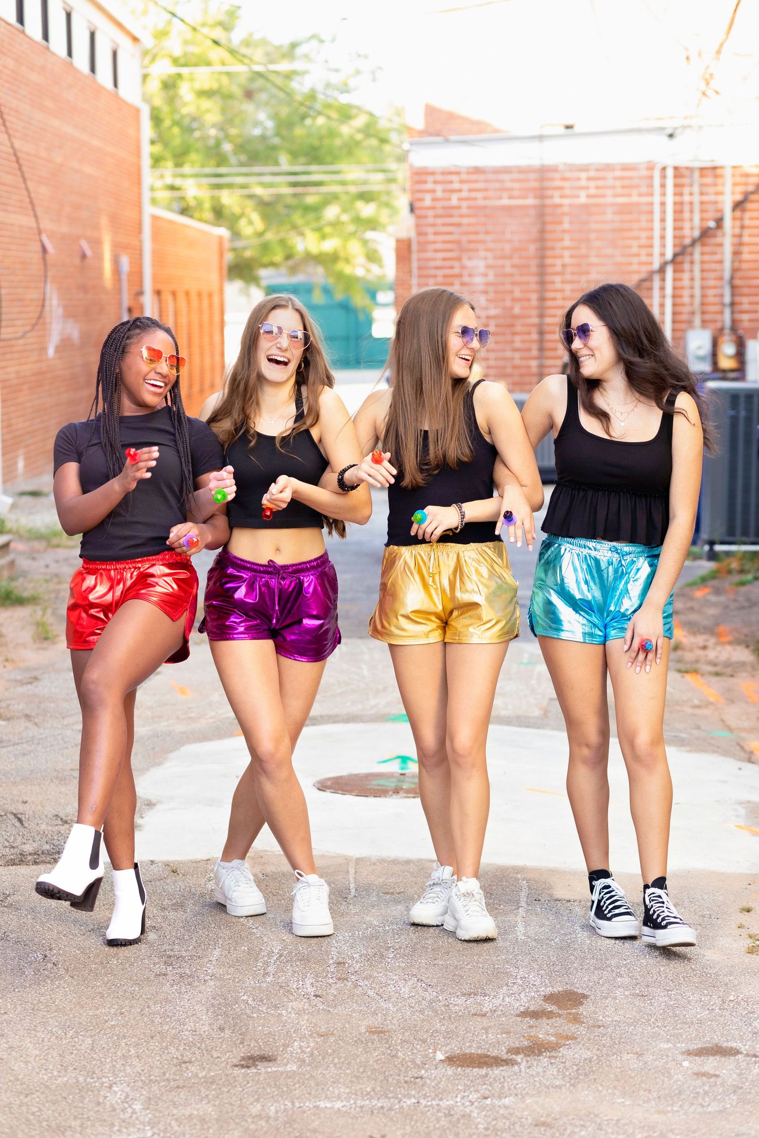 Group wearing colorful metallic shorts and black tops showing off dance poses in an outdoor setting.