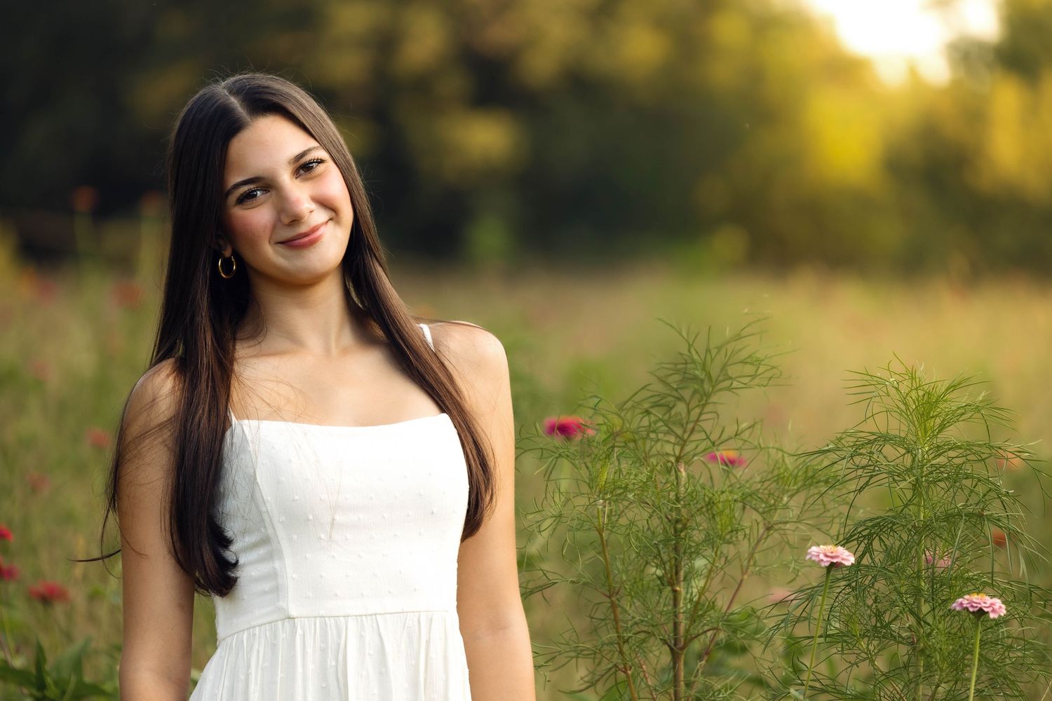 Woman in white dress standing in wild meadow at sunset.