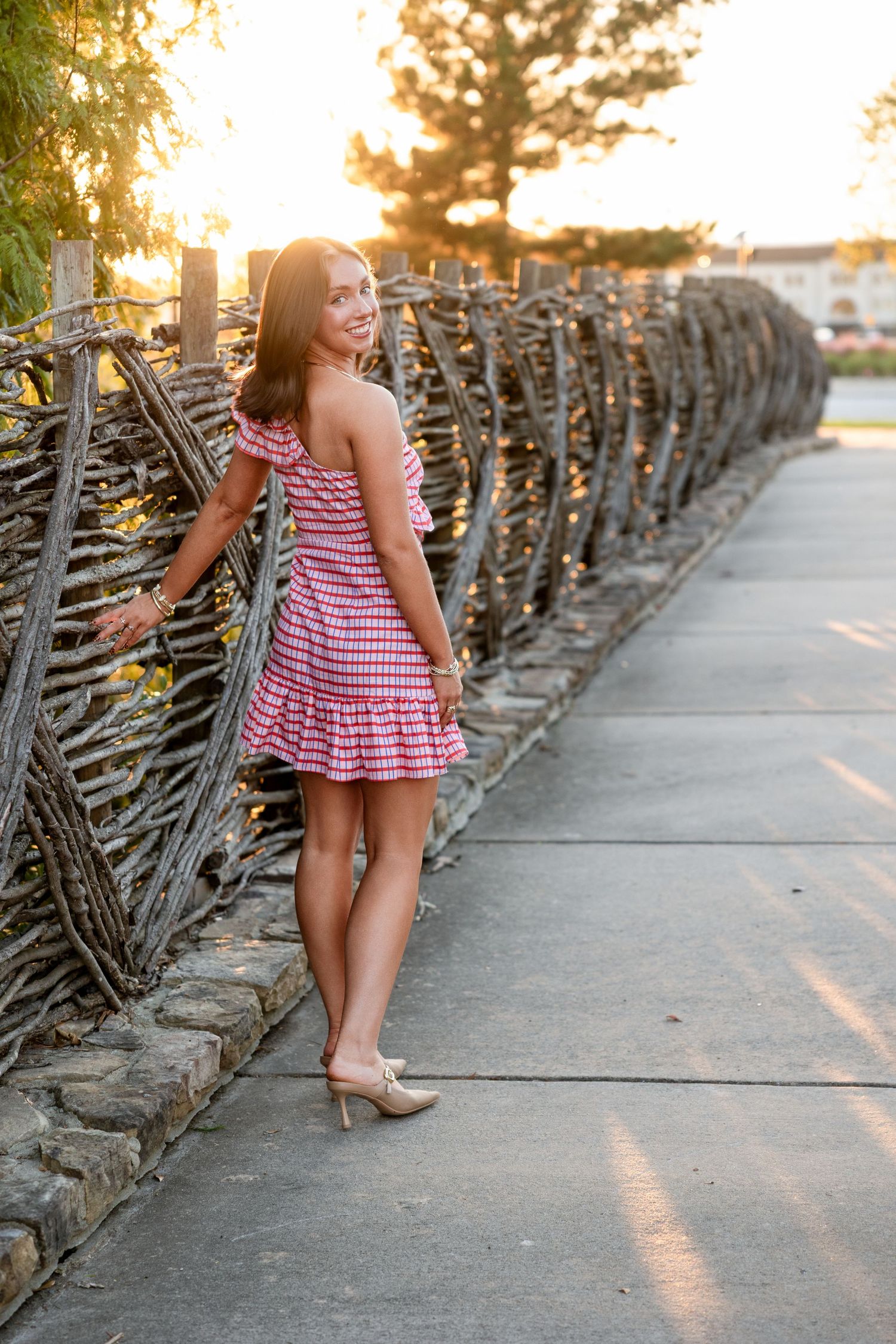 A child in a red and white striped dress walks along a wrought iron fence during golden hour sunset.