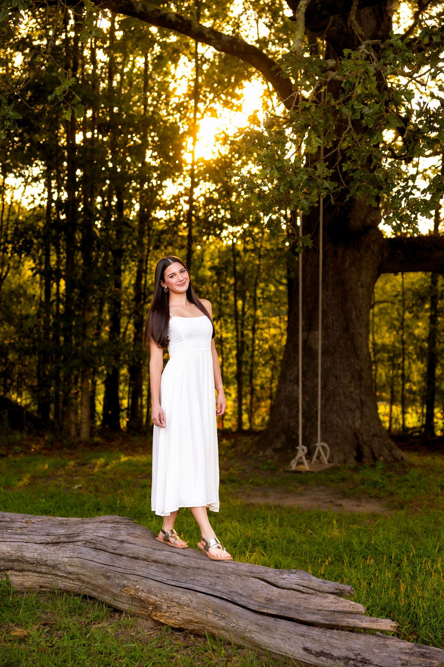 A white dress contrasts beautifully against a golden sunset in a wooded forest setting with a fallen log.