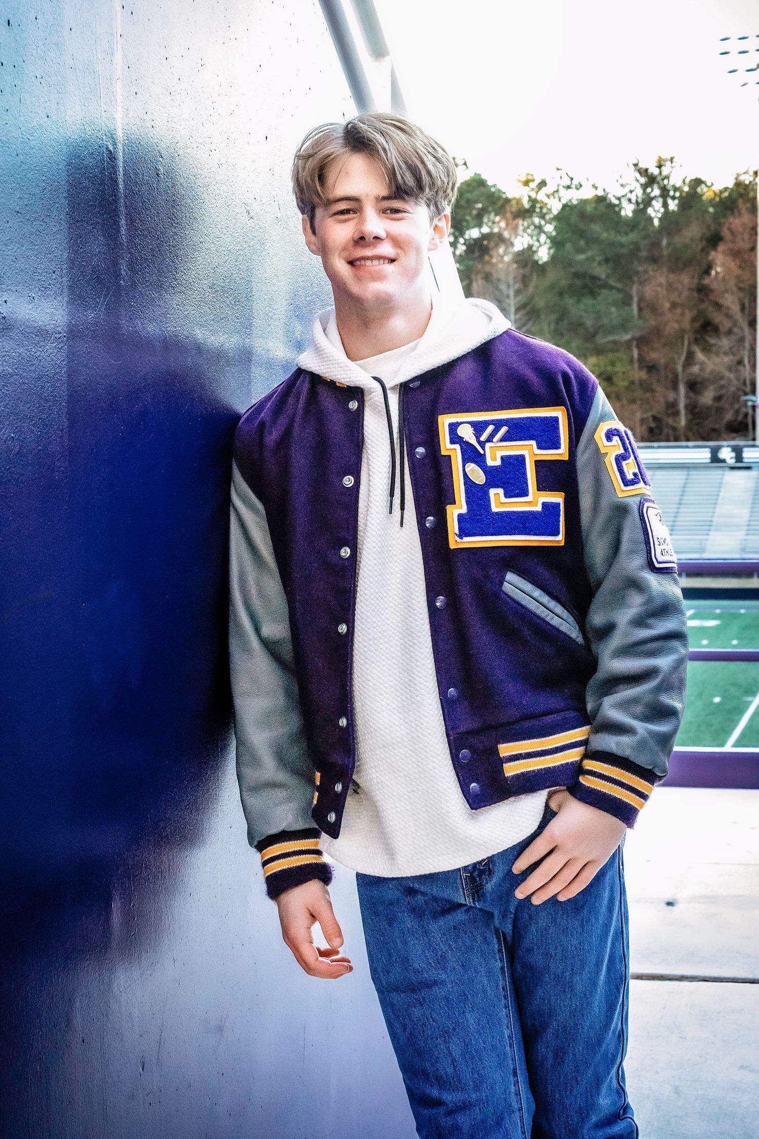 Person wearing varsity letterman jacket and jeans posing against blue background.