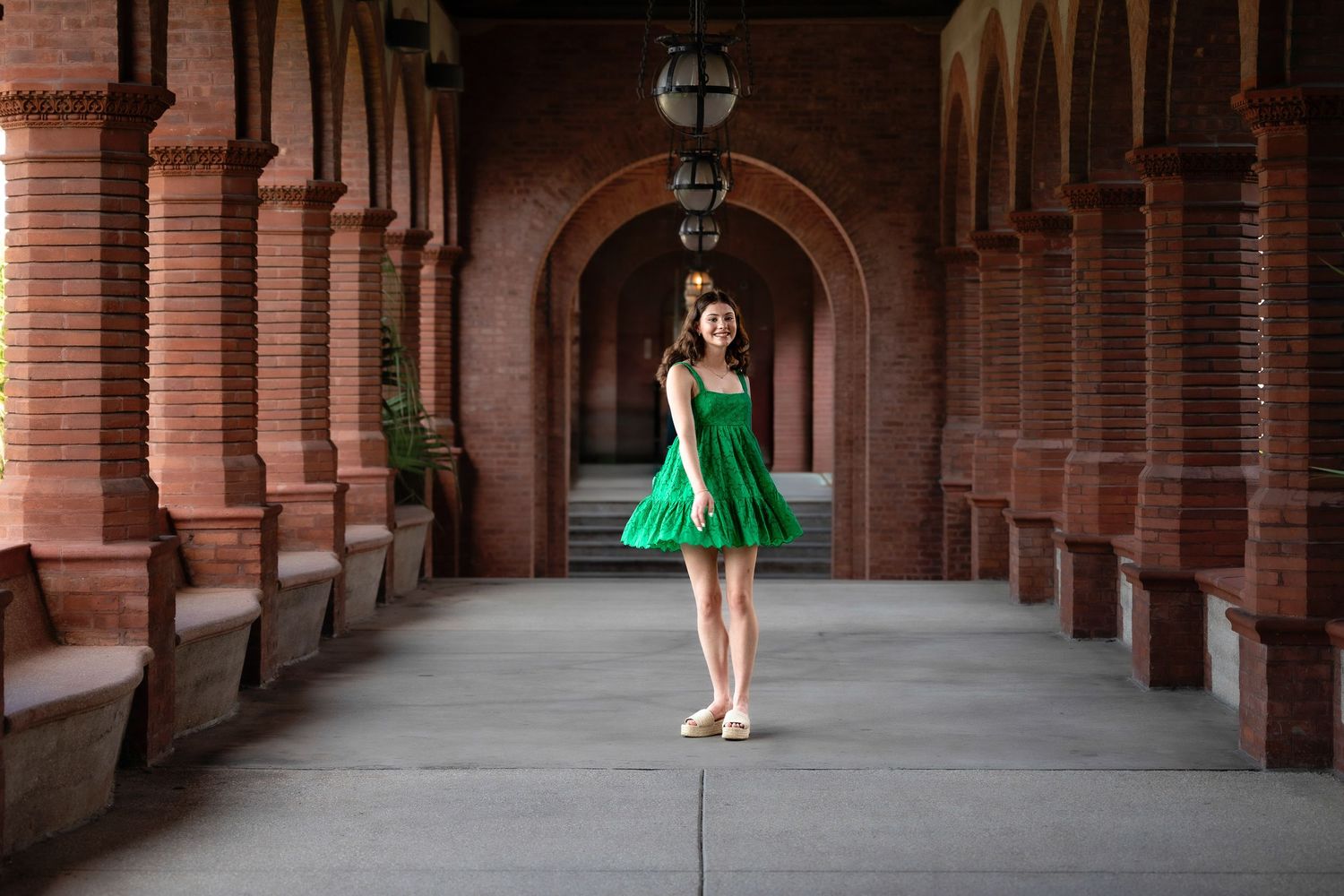 Figure in emerald green dress walking through elegant brick archway corridor.