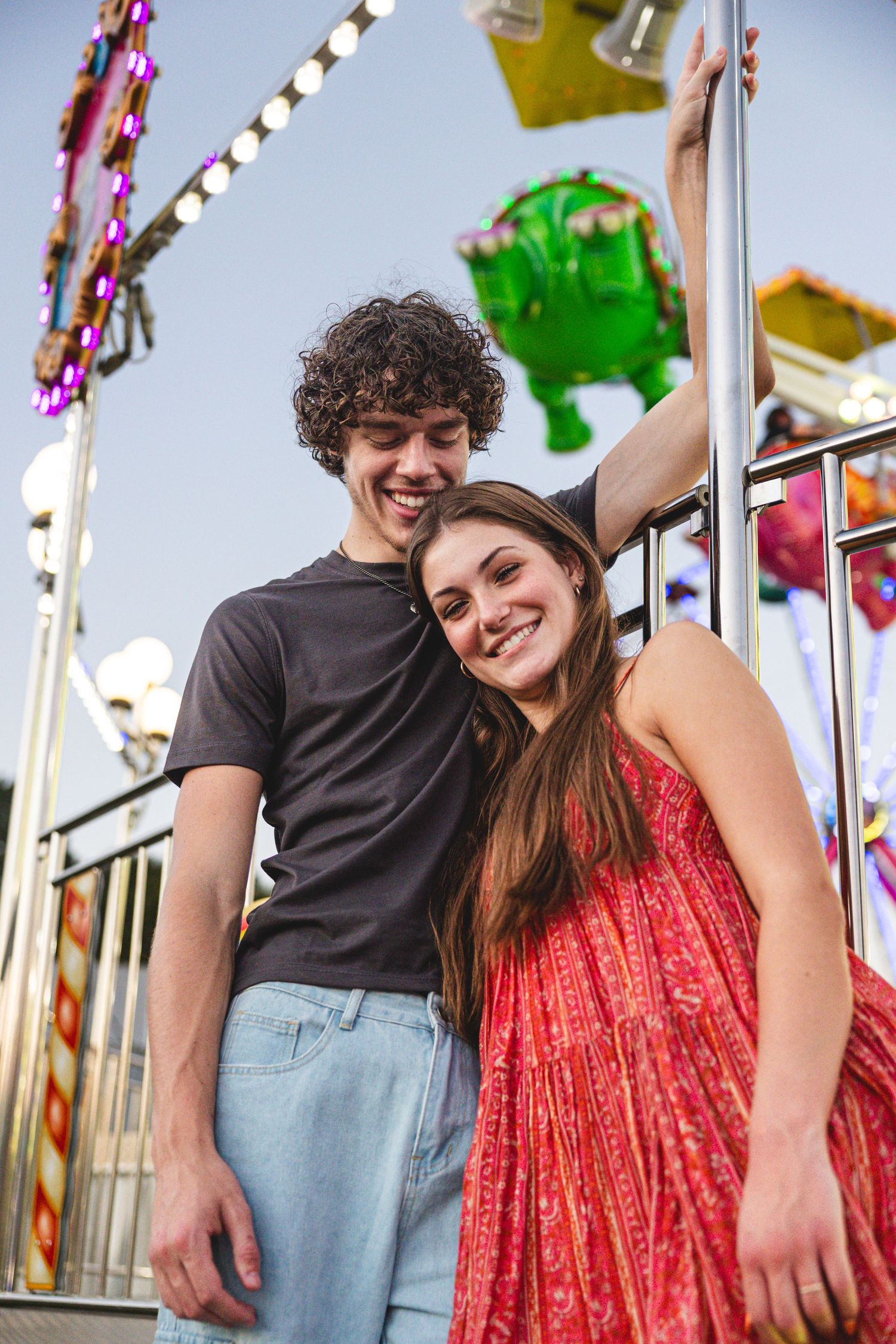Couple in casual attire sharing intimate moments at a carnival with colorful lights.